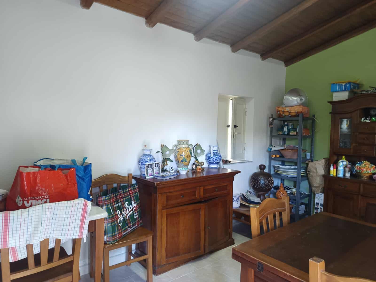 Una stanza con mobili in legno, decorazioni e oggetti vari, ideale per la vendita o l'affitto di immobili residenziali, con pareti bianche e un soffitto in legno.