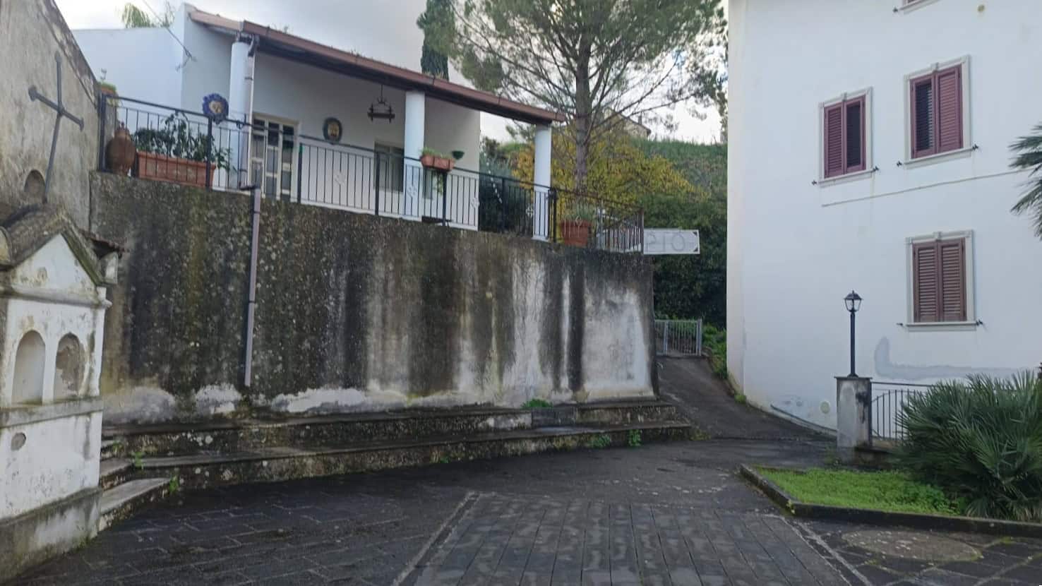 Veduta di strada in pietra con case tradizionali e vegetazione, in un contesto rurale tranquillo, ideale per immobili in vendita o affitto in zone storiche italiane.