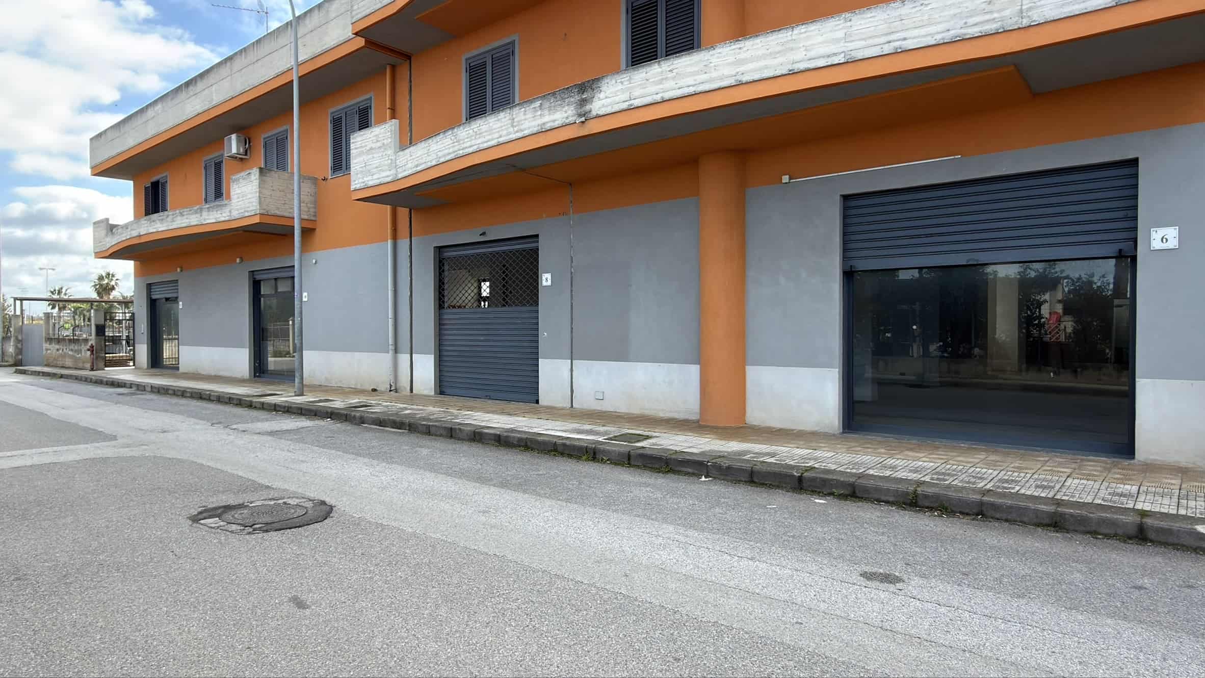 Ampio negozio commerciale con vetrine e ingresso su strada, situato in zona urbana con parcheggio adiacente, ideale per attività commerciali e uffici.