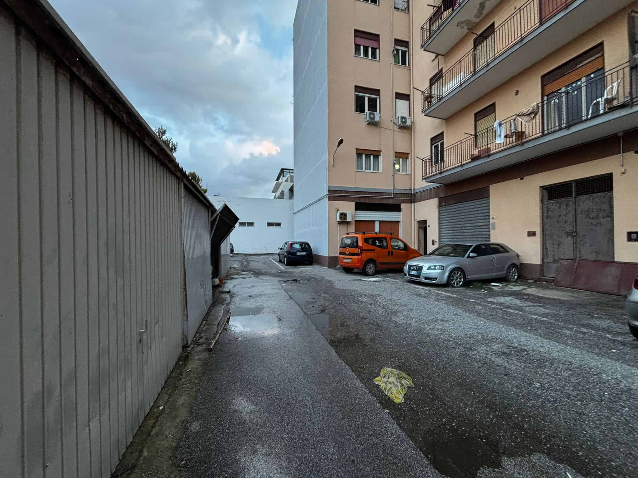 Auto in sosta davanti a un edificio residenziale con balconi, in un'area urbana con strada asfaltata e cielo nuvoloso, in Italia.