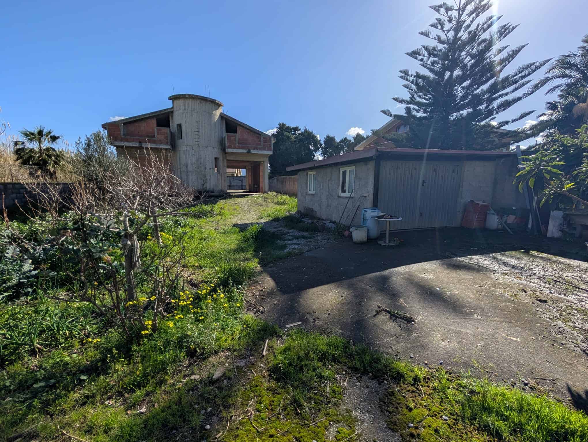 Pannello solare e giardino in un cortile di una casa in stile rustico con alberi e vegetazione rigogliosa, sotto un cielo sereno.
