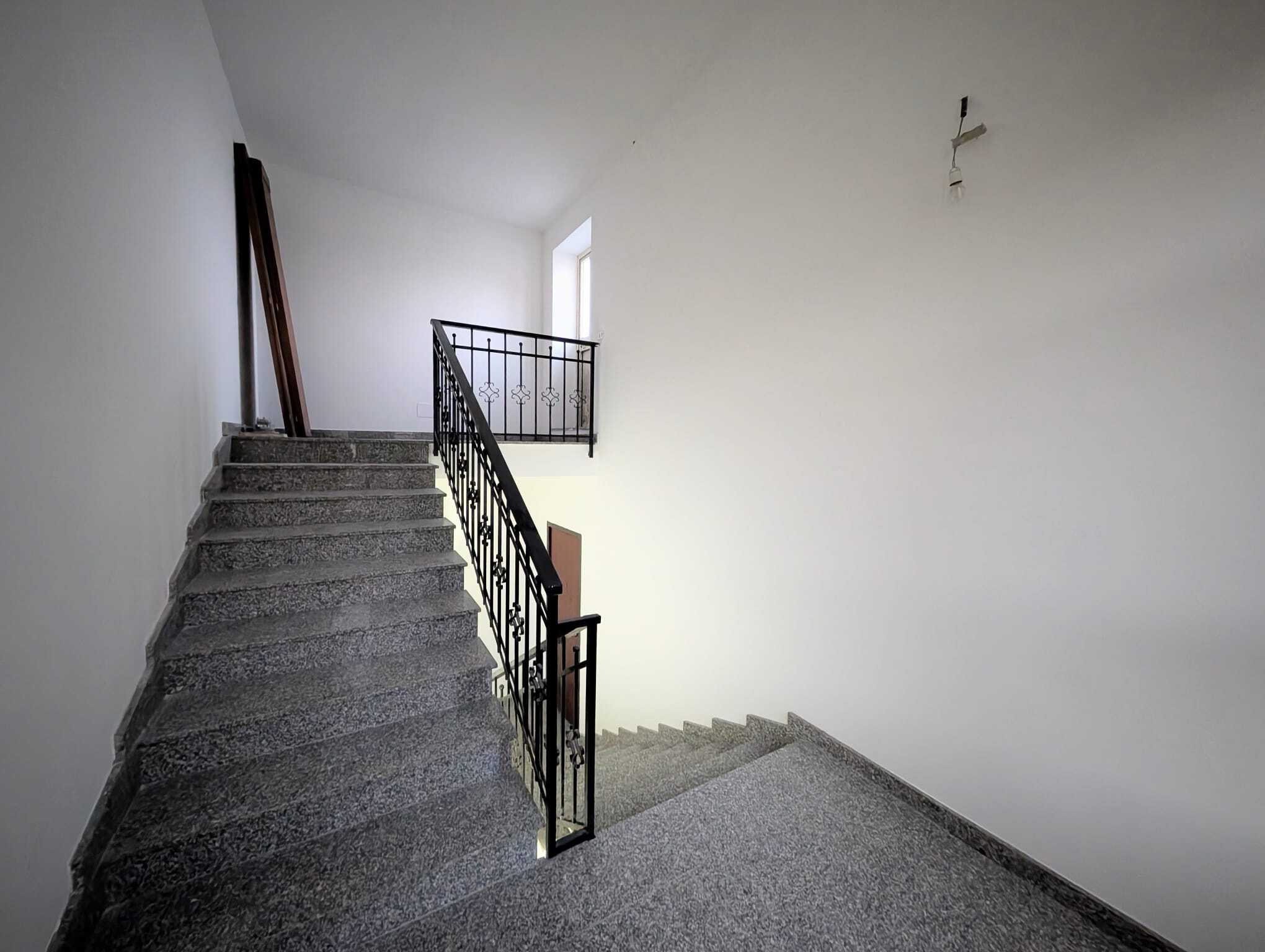 Escalier interno in edificio residenziale con pareti bianche e ringhiera in metallo, illuminato da luce naturale proveniente da una finestra. Ideale per ambienti moderni e funzionali.
