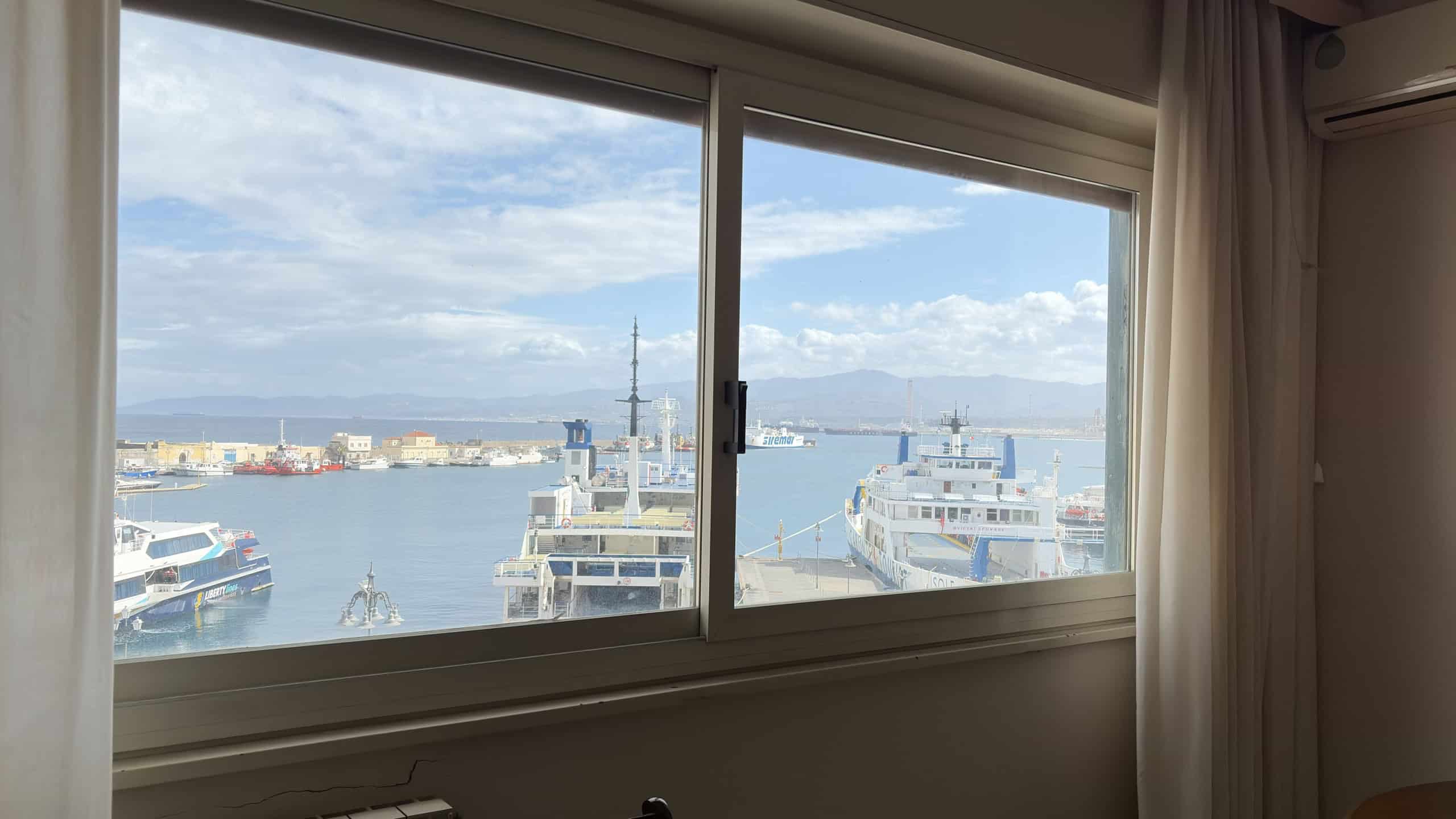 Vista panoramica del porto di Napoli con barche e navi, vista da una finestra di un appartamento, con cielo sereno e nuvole sparse, ideale per immobili con vista mare in vendita o affitto.