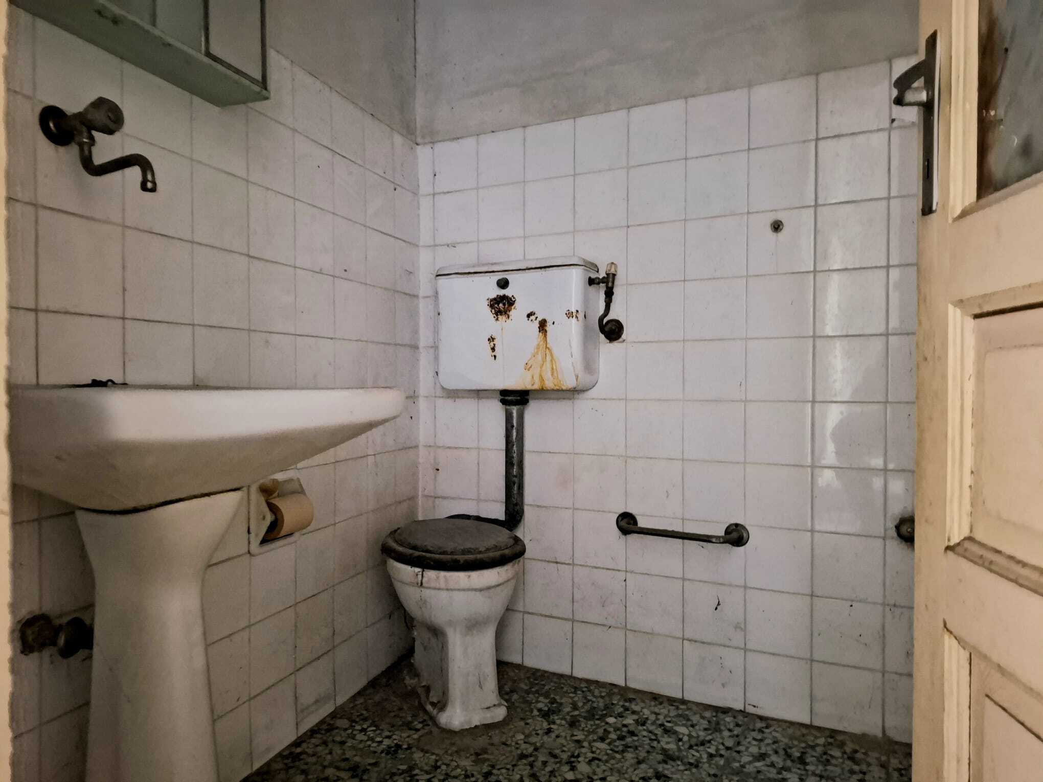 Il bagno vecchio e trascurato con sanitari rotti e pareti in piastrelle bianche usurate, pronto per una ristrutturazione completa.
