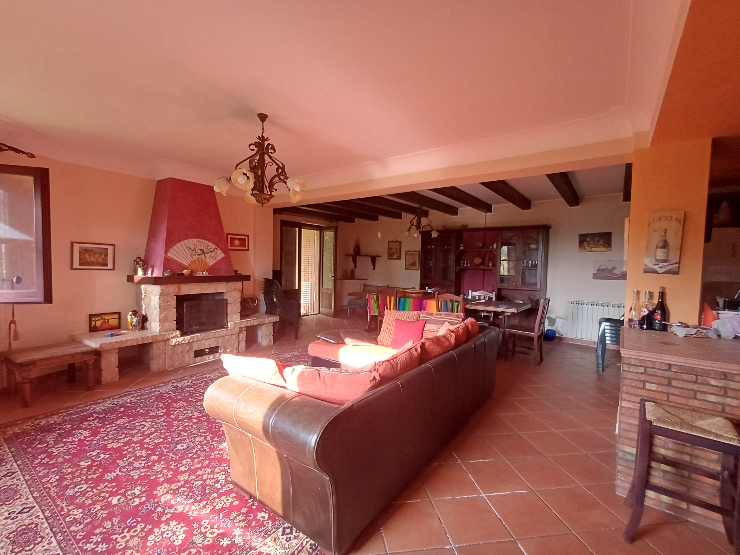 Ampio soggiorno con camino, divano in pelle, tavolo da pranzo e decorazioni rustiche in una casa in vendita a Ficarra, Me.