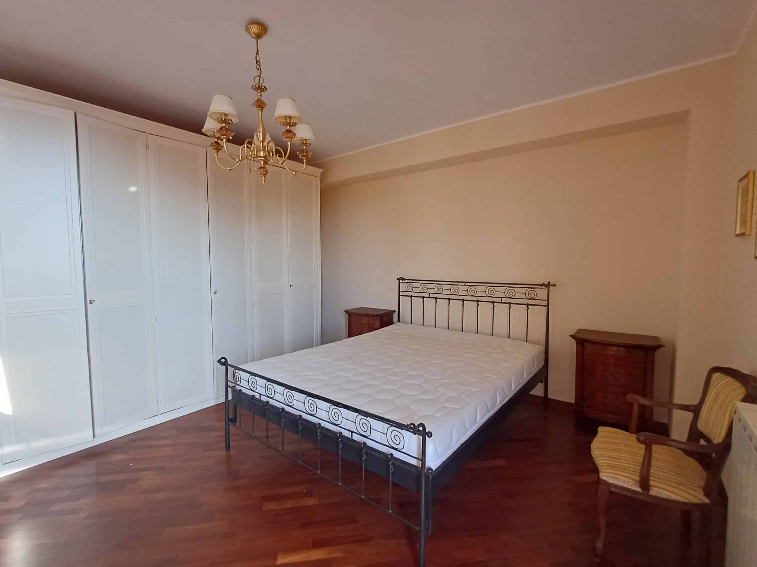 Camera matrimoniale spaziosa con armadio a muro, letto in ferro battuto e sedie in legno, in una casa indipendente a Ficarra, Me.