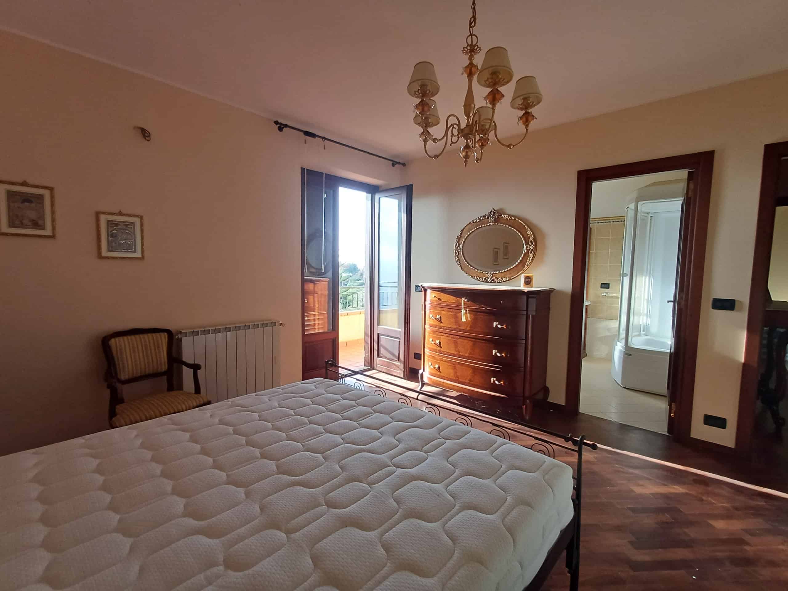Camera da letto spaziosa con letto matrimoniale, armadio antico e accesso al balcone con vista panoramica a Ficarra, Messina.