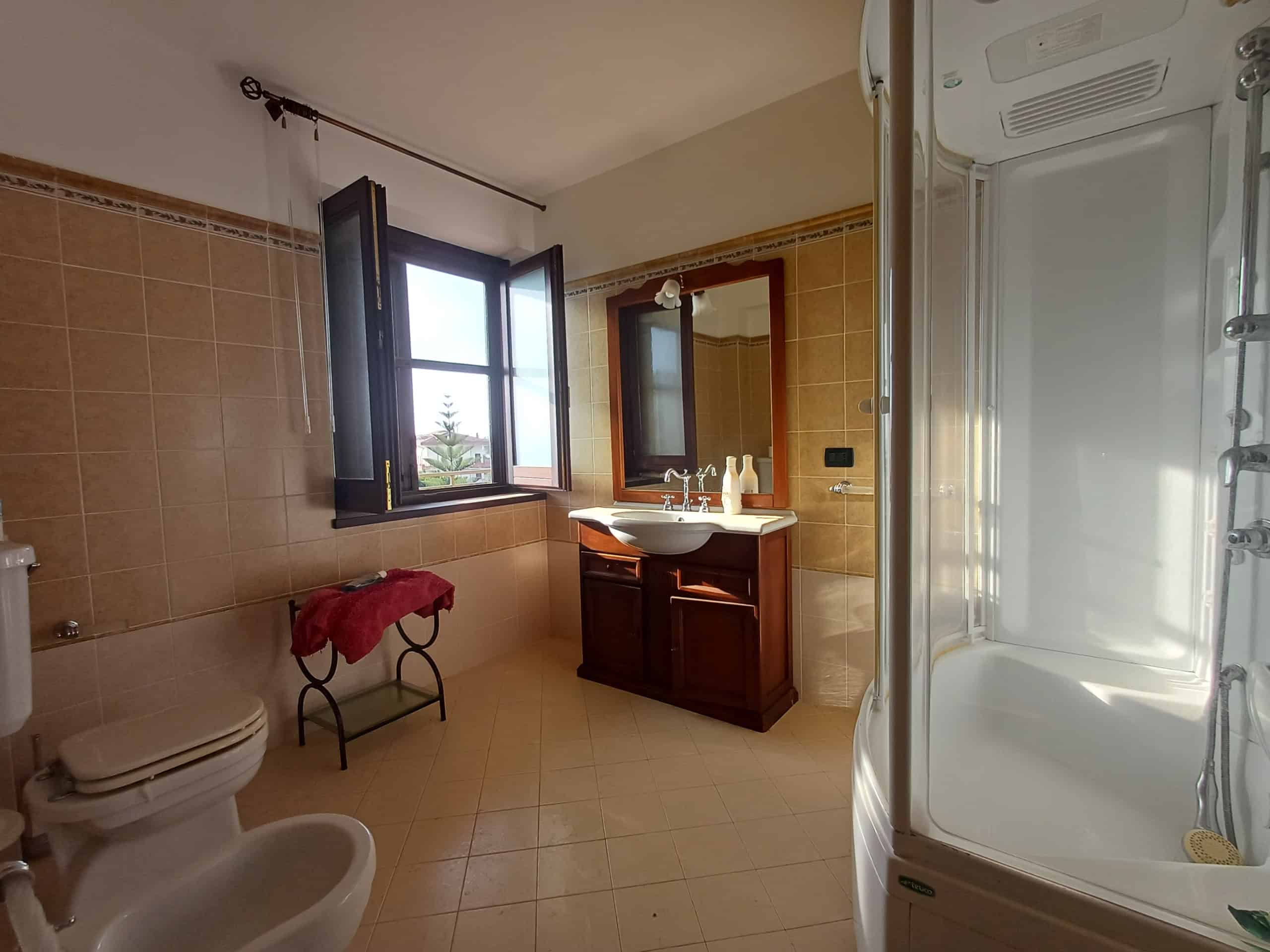 Bagno luminoso con finestra aperta, lavabo, specchio e doccia moderna in casa a Ficarra.