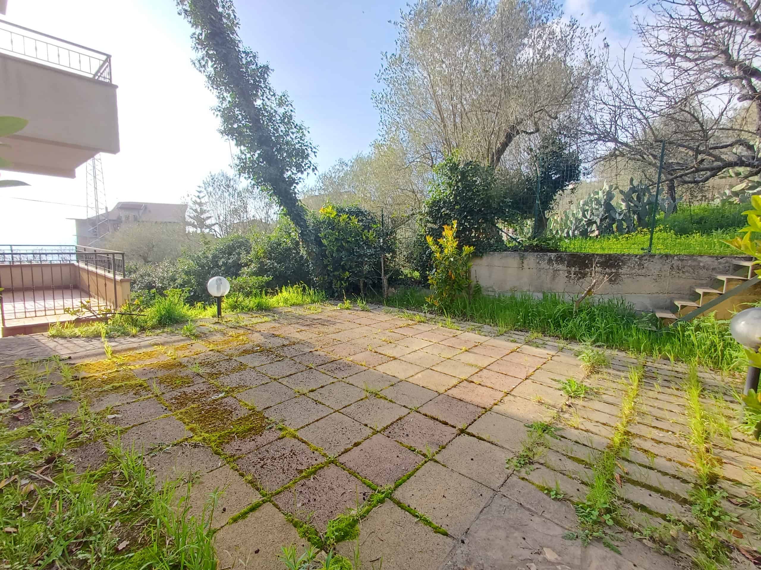 Spazio esterno di una casa indipendente a Ficarra con pavimentazione in pietra e vegetazione circostante, ideale per relax e attività all'aperto.