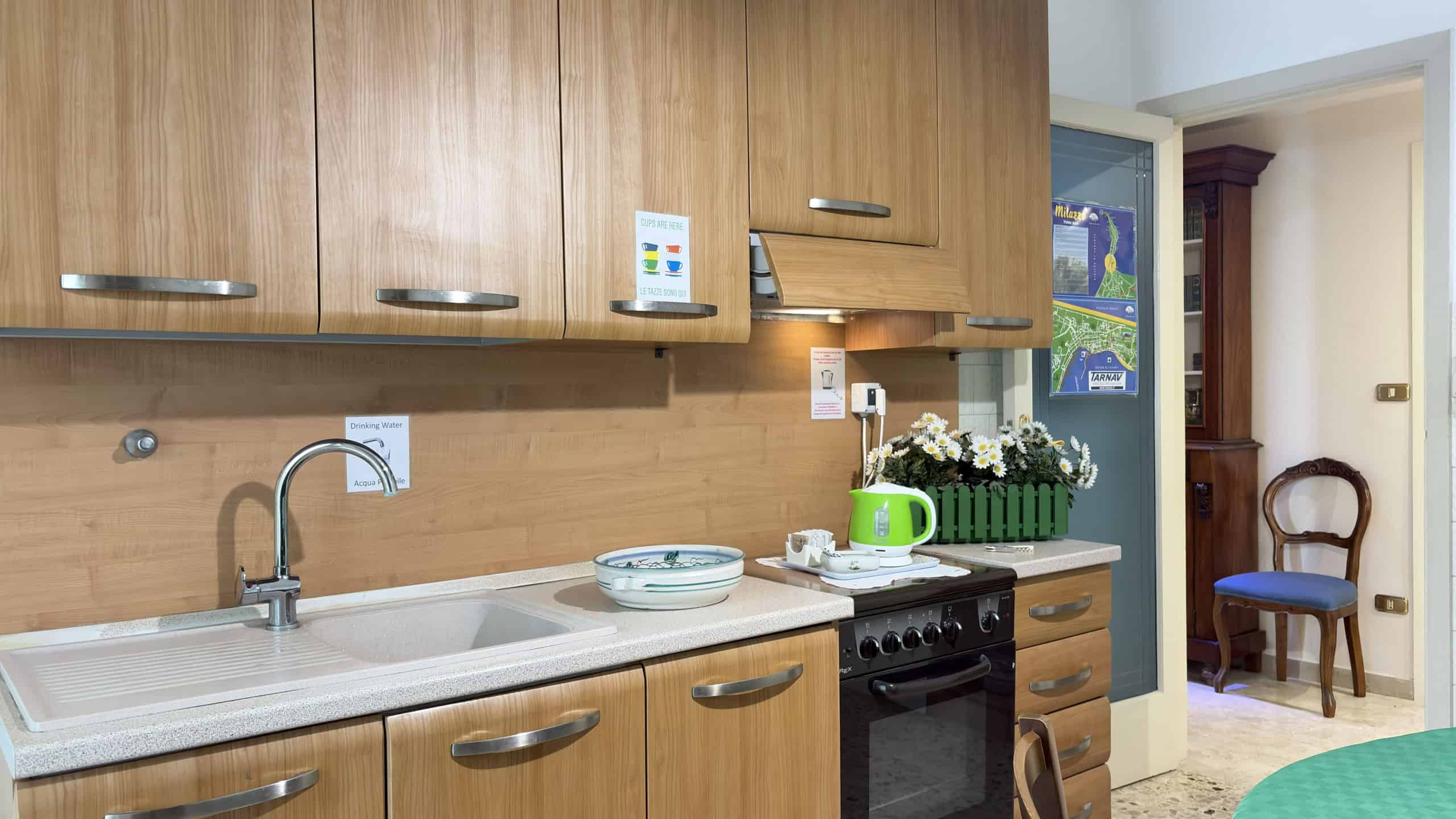 Esterno di una cucina moderna con mobili in legno, lavello, piano cottura e decorazioni floreali, ideale per case e appartamenti in vendita o affitto a NextCasa.