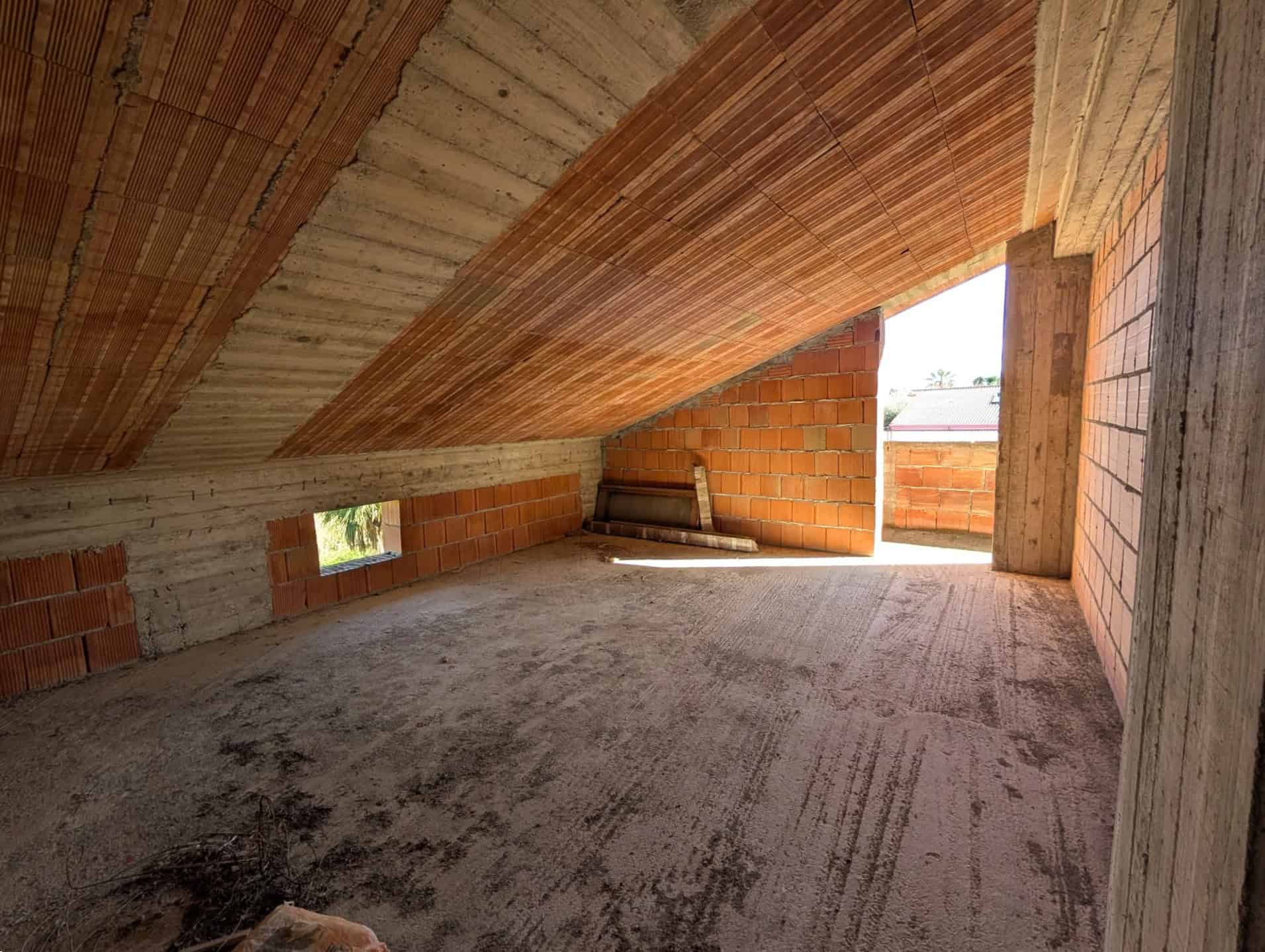 Pannello di soffitta in costruzione con pareti in mattoni e soffitto in cemento armato, spazio ancora da rifinire, illuminato dalla luce naturale proveniente da una finestra e un'apertura sul lato.