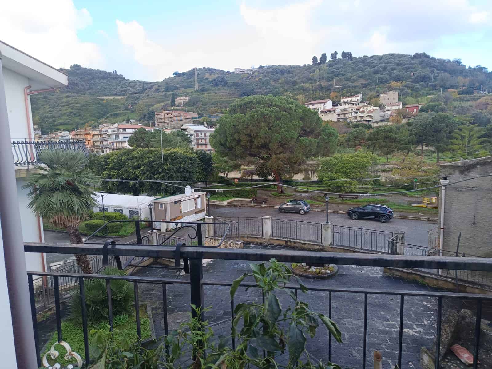 Ampia vista panoramica su un paesaggio collinare con alberi e case, vista da un balcone con ringhiera in ferro battuto, in un contesto residenziale tranquillo e verdeggiante.