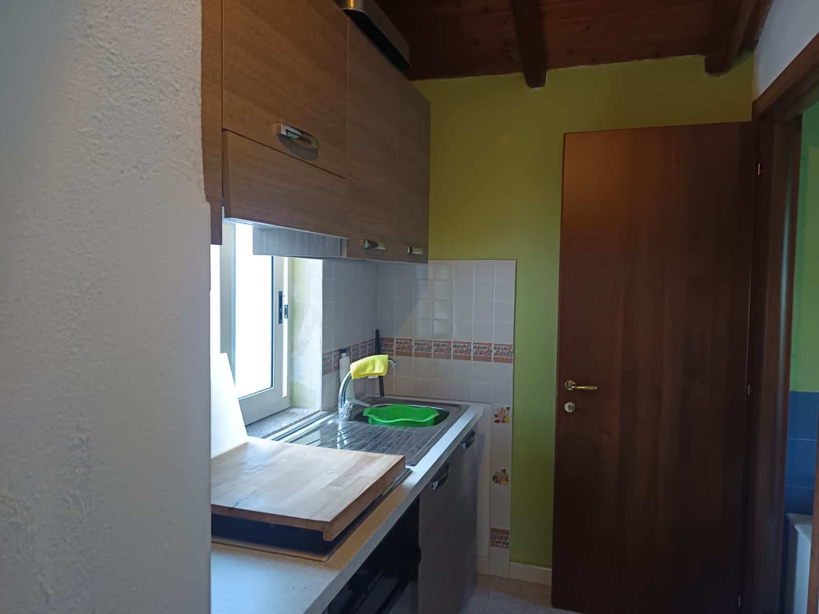 Lavandino da cucina con finestra, piano di lavoro in legno e armadietti in legno chiaro, ambiente luminoso e accogliente, ideale per cucinare e preparare pasti in casa.