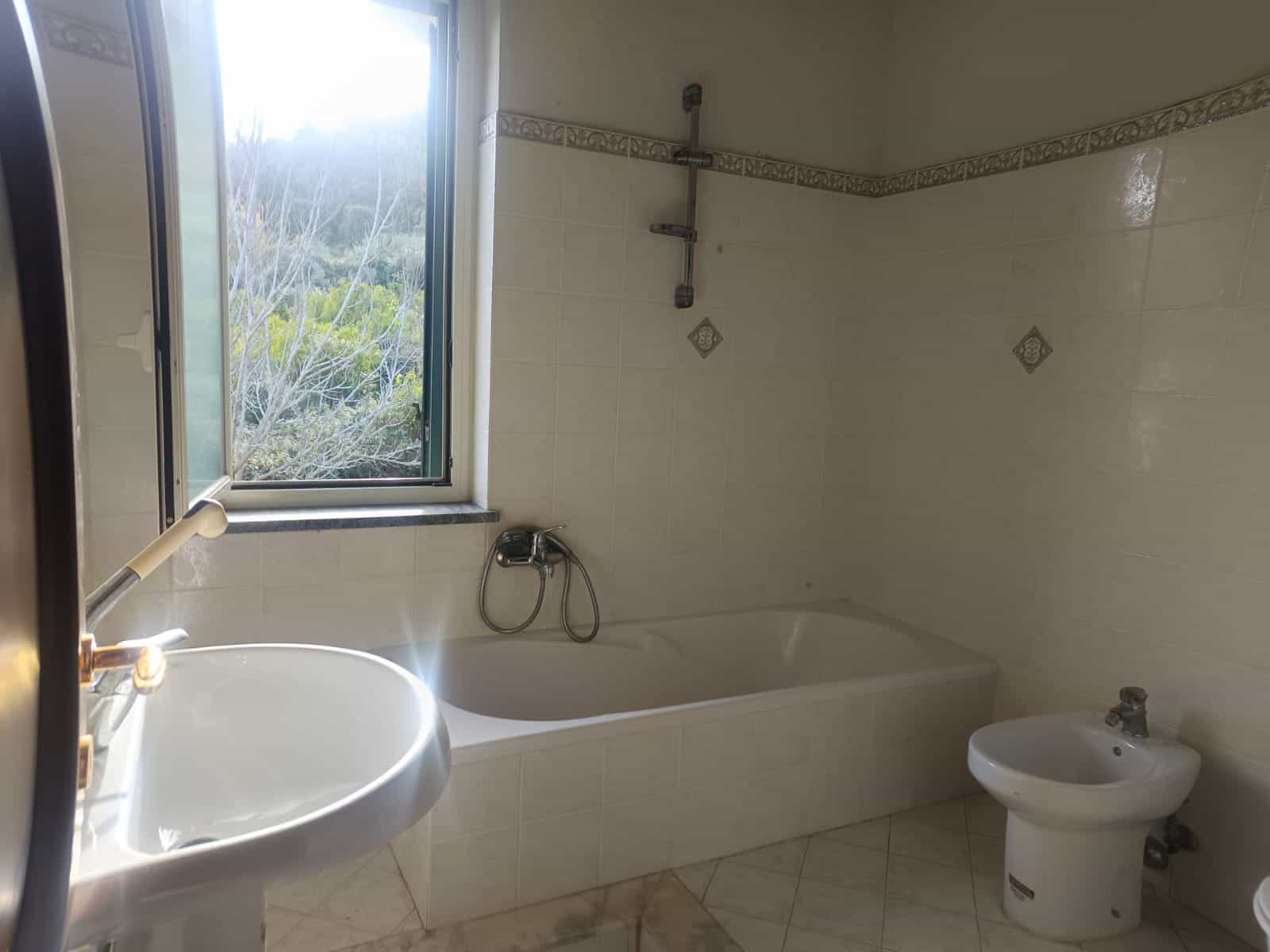 Lavabo e vasca da bagno in un bagno luminoso con finestra, piastrelle chiare e accessori essenziali, ideale per un'abitazione moderna e funzionale.