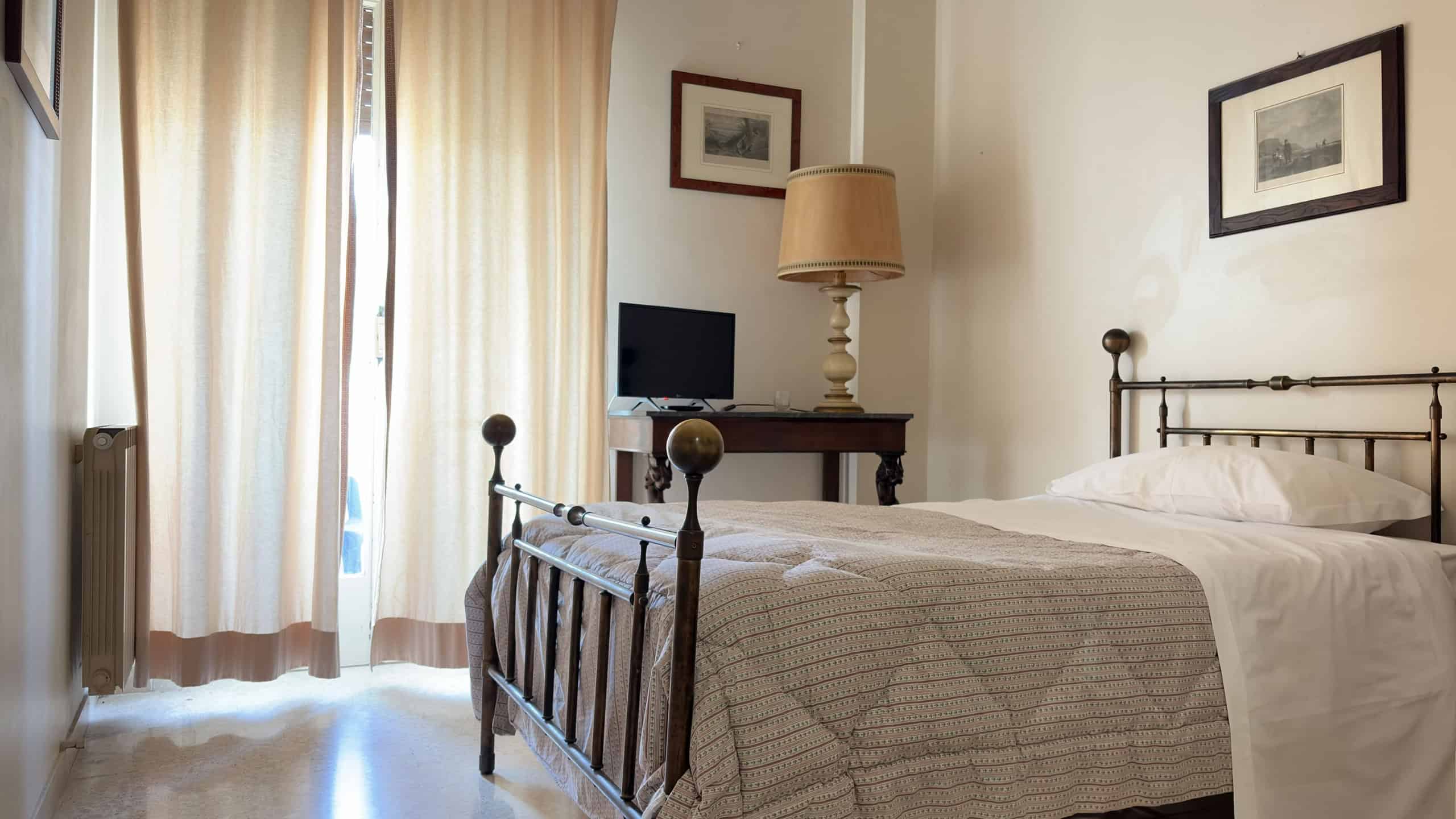 Elegante camera da letto con letto in ferro battuto, tende leggere e decorazioni artistiche alle pareti, ambiente accogliente e luminoso, ideale per soggiorni confortevoli.