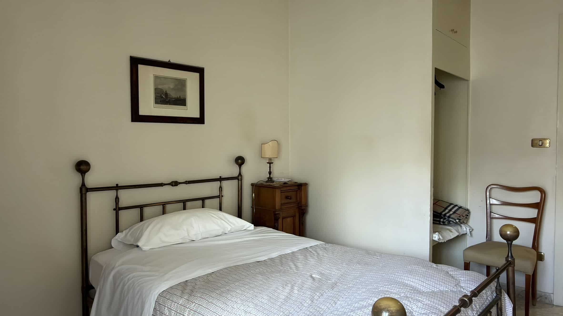 Elegante camera da letto con letto in ferro battuto, comodino in legno e lampada da tavolo, ambiente accogliente e luminoso, ideale per soggiorni rilassanti in una casa moderna.
