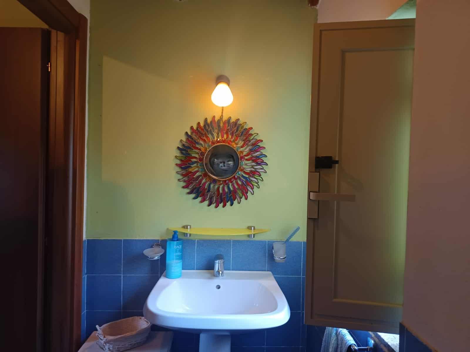 Lavabo da bagno con specchio decorativo colorato e illuminazione, ambiente domestico accogliente e luminoso.