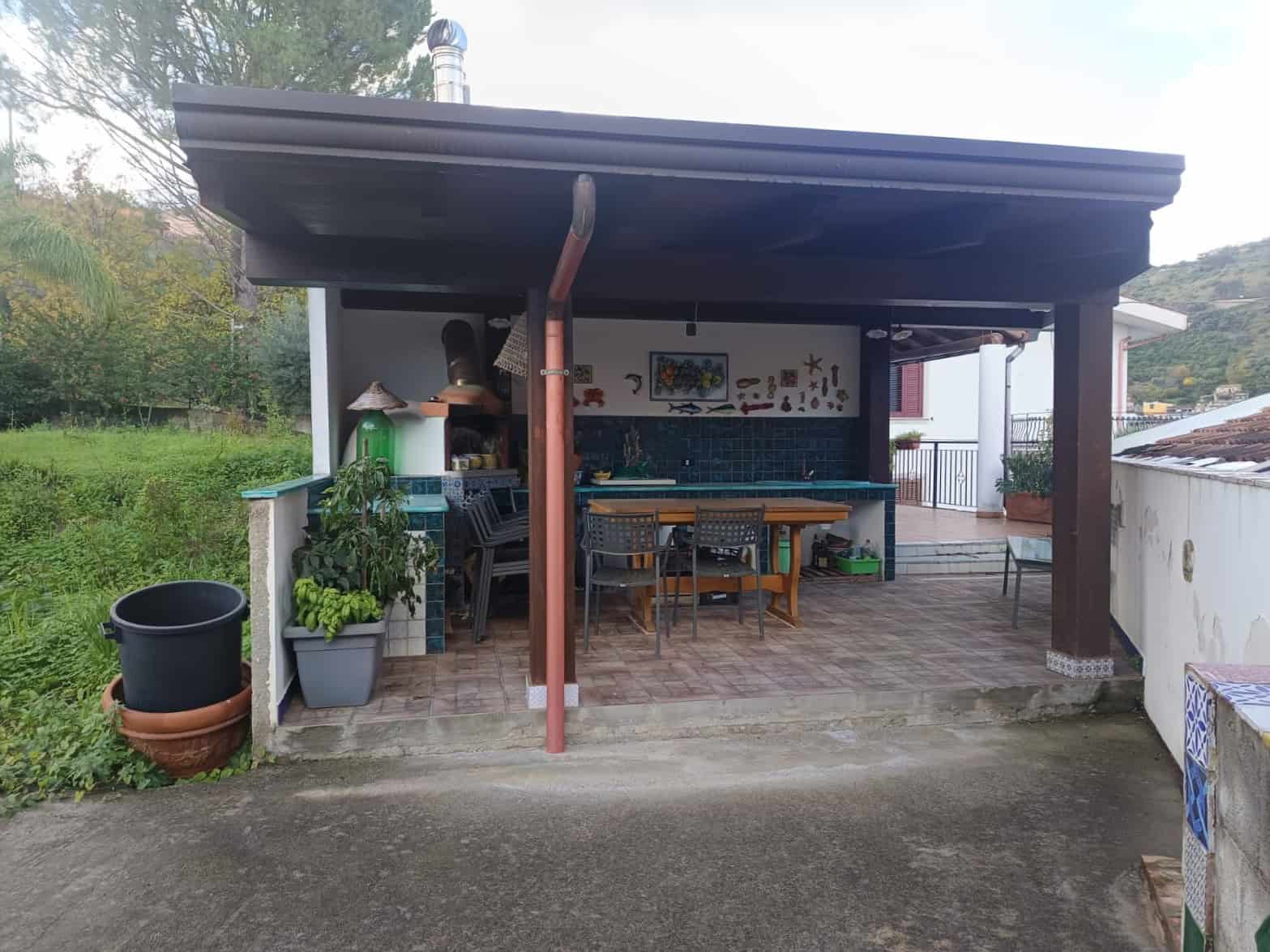Aggiungi un'area coperta con tavolo e sedie per pranzi all'aperto, decorata con piante e oggetti artistici, ideale per momenti di relax e convivialità in giardino.