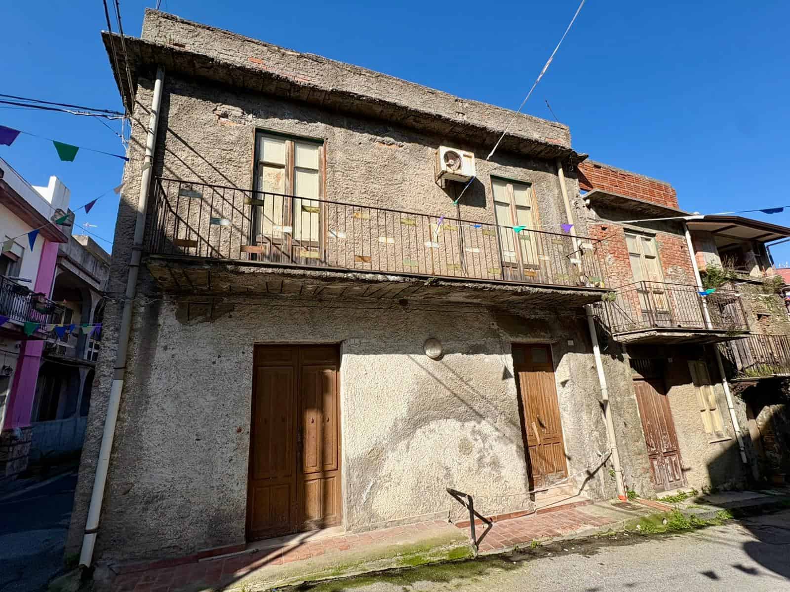 Antico edificio residenziale in pietra con balcone in ferro battuto e finestre con infissi in legno, situato in un quartiere storico di città.