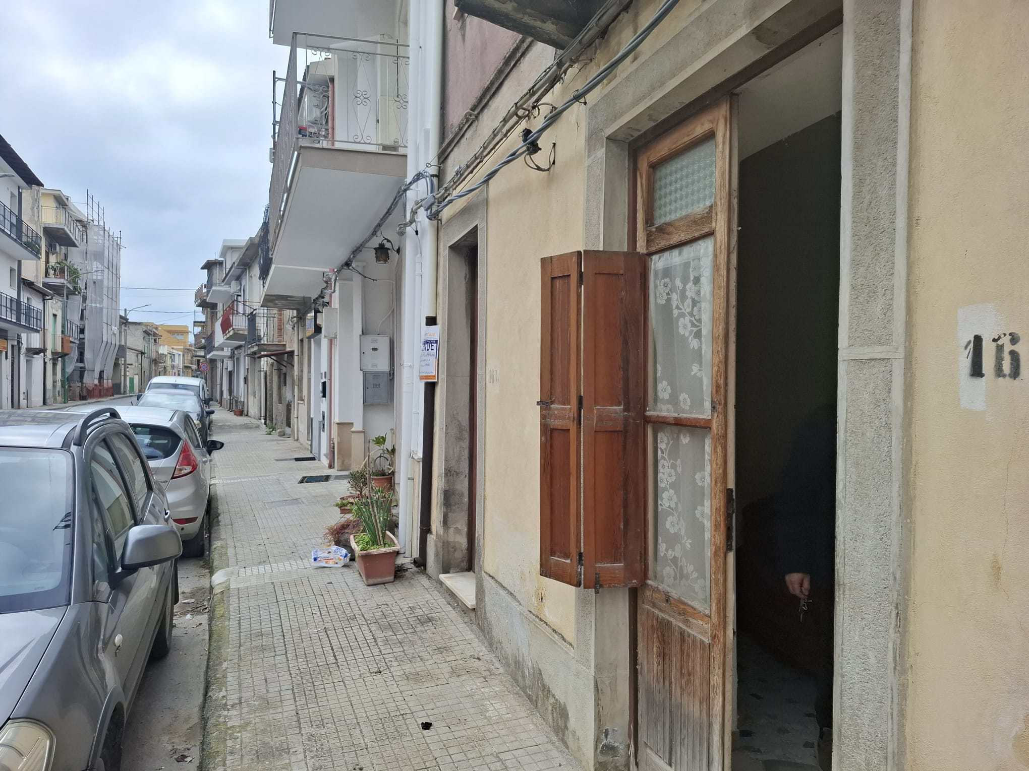 Vista di una strada urbana con edifici residenziali, auto parcheggiate e una porta aperta in un edificio storico, in un quartiere tranquillo di città.