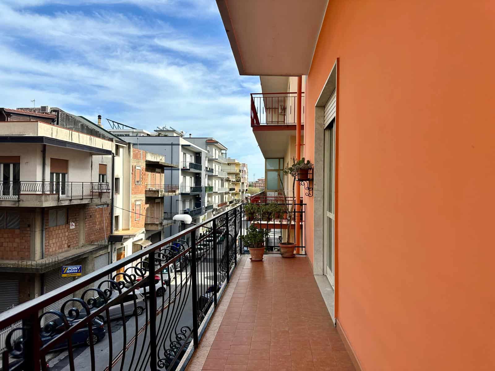 Balcone di un appartamento con vista su edifici residenziali e cielo sereno, con piante e ringhiera in ferro battuto, ideale per godersi l'aria aperta e il panorama urbano.