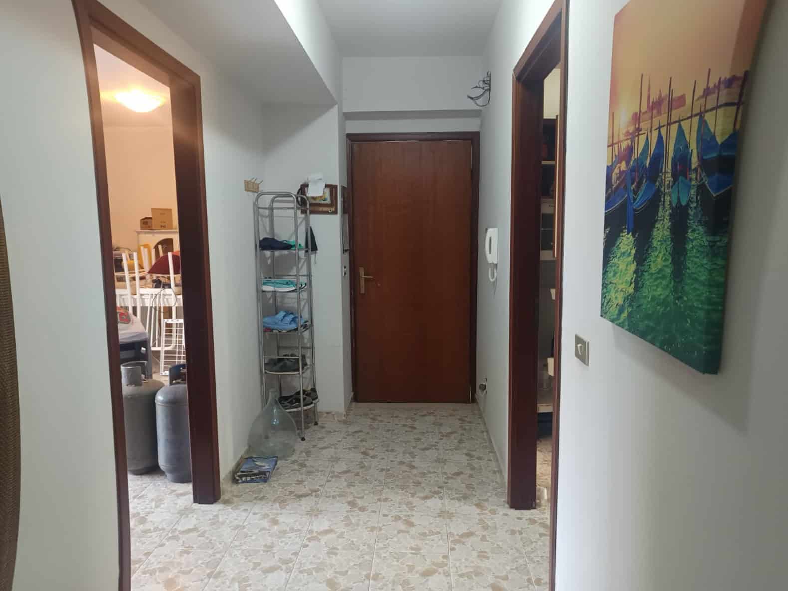 Un cancello di ingresso in un appartamento con pareti bianche, pavimento in piastrelle beige, porta in legno e decorazioni artistiche alle pareti, ambiente luminoso e accogliente.