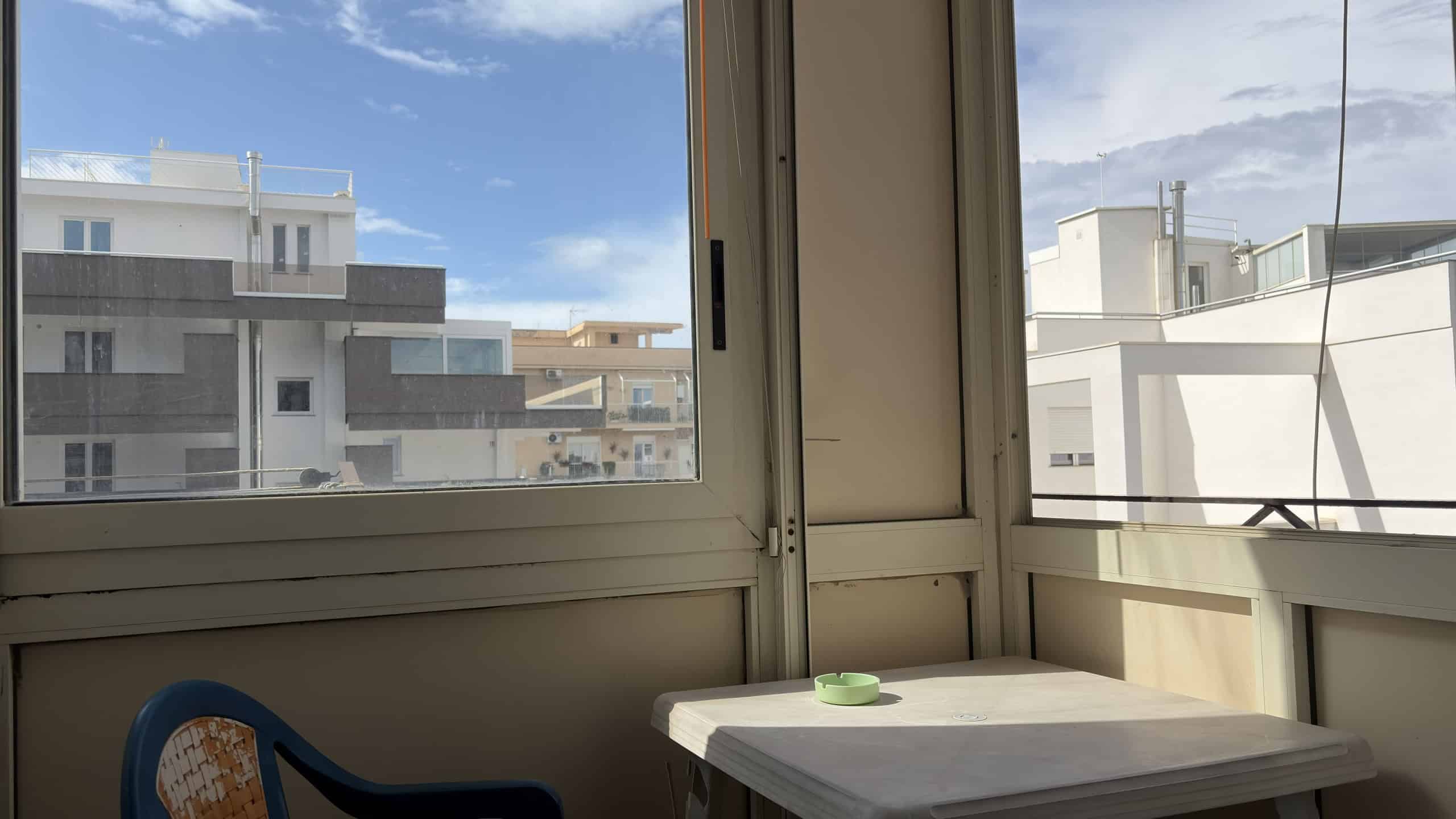Vista panoramica di un balcone con ampie finestre che offrono una vista su edifici moderni e il cielo sereno, ideale per relax e momenti di convivialità all'aperto.