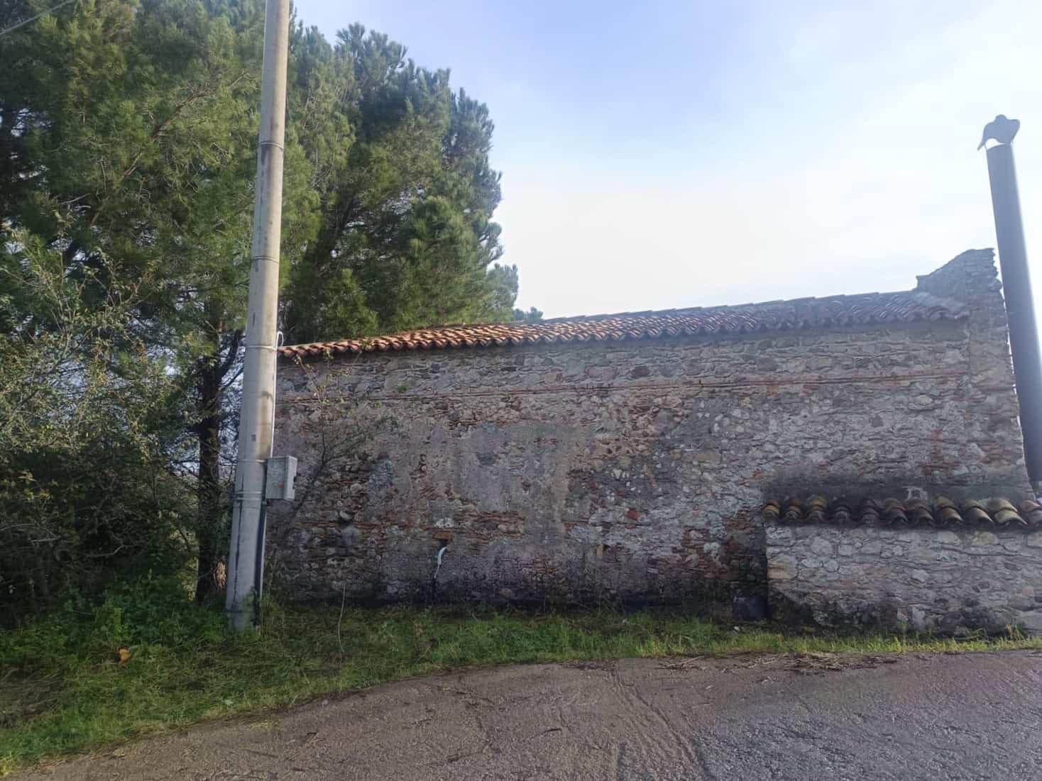Una parete in pietra di un edificio rurale con vegetazione circostante, situata in un'area tranquilla e naturale.