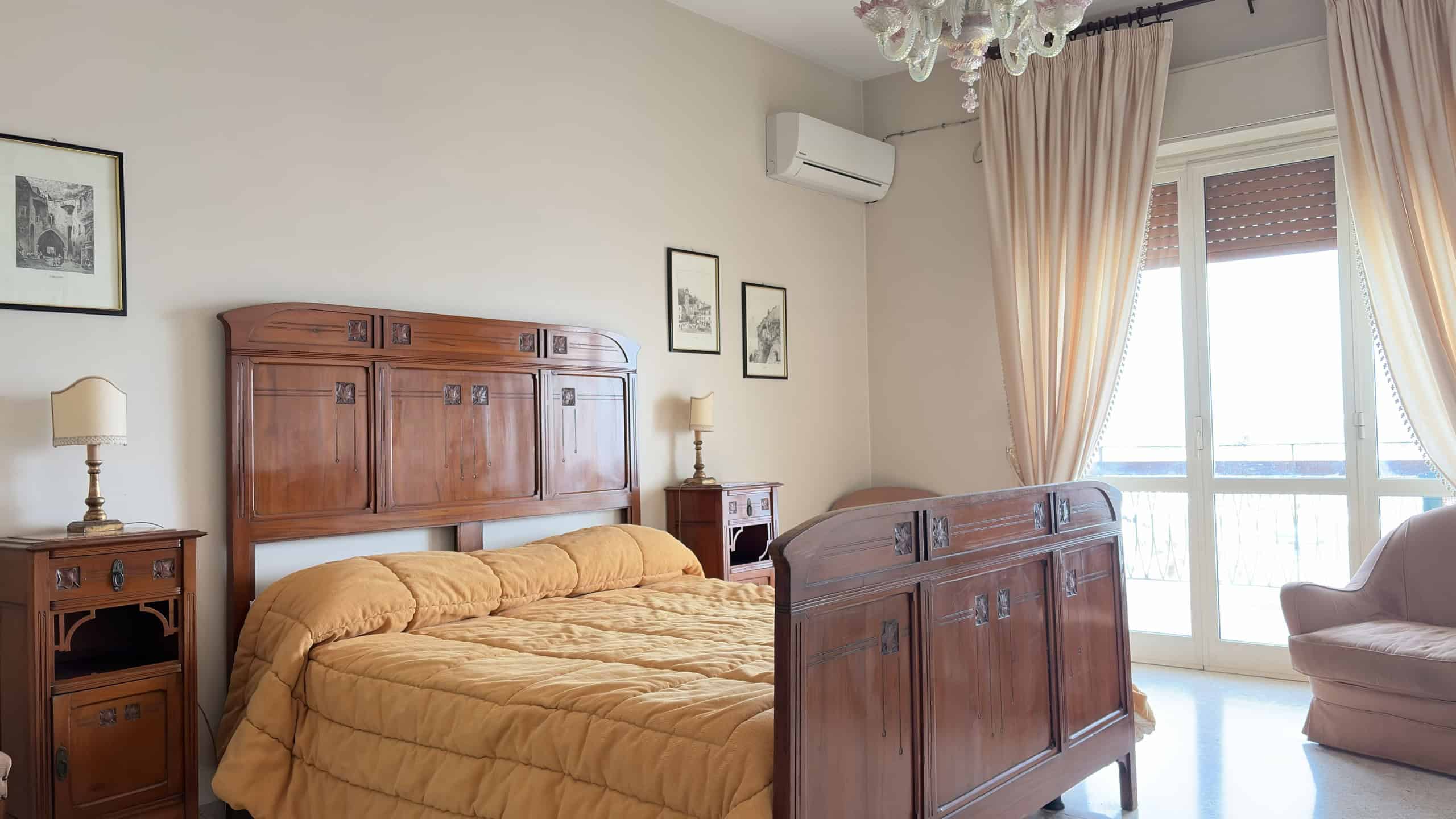 Ampio soggiorno con letto matrimoniale in legno, aria condizionata e grande finestra con tende beige, ideale per relax e comfort.