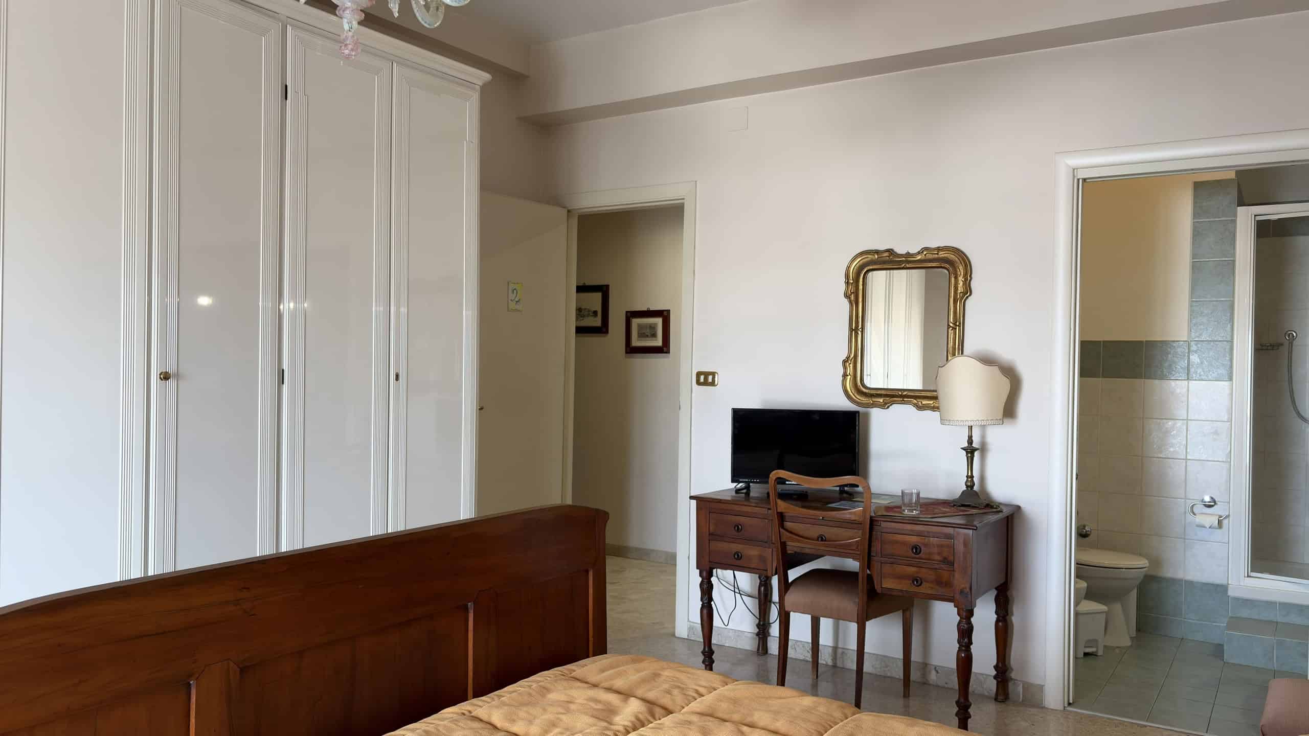 Elegante camera da letto con armadio a muro bianco, scrivania in legno e specchio dorato, ambiente luminoso e accogliente, ideale per vivere momenti di relax e comfort.