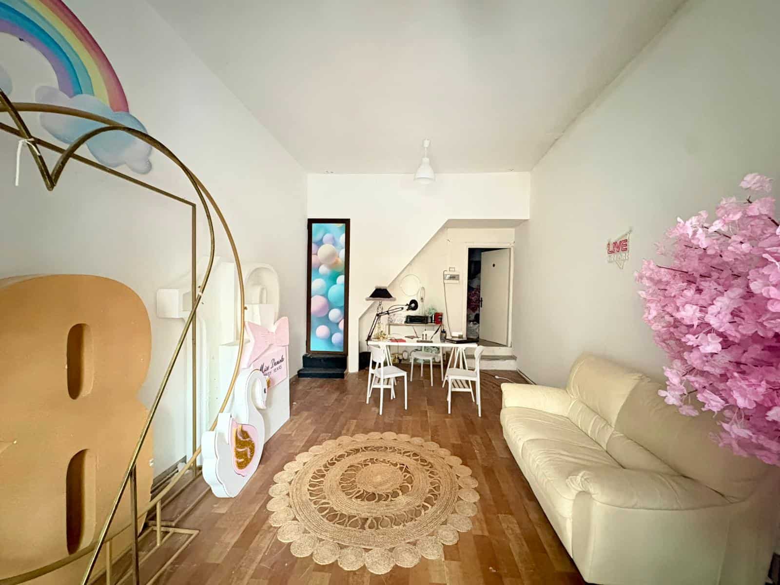 Un ambiente accogliente e luminoso con decorazioni colorate, divano beige, tappeto rotondo in tessuto, e dettagli decorativi come arcobaleno e fiori di ciliegio rosa, ideale per uno spazio di relax e.