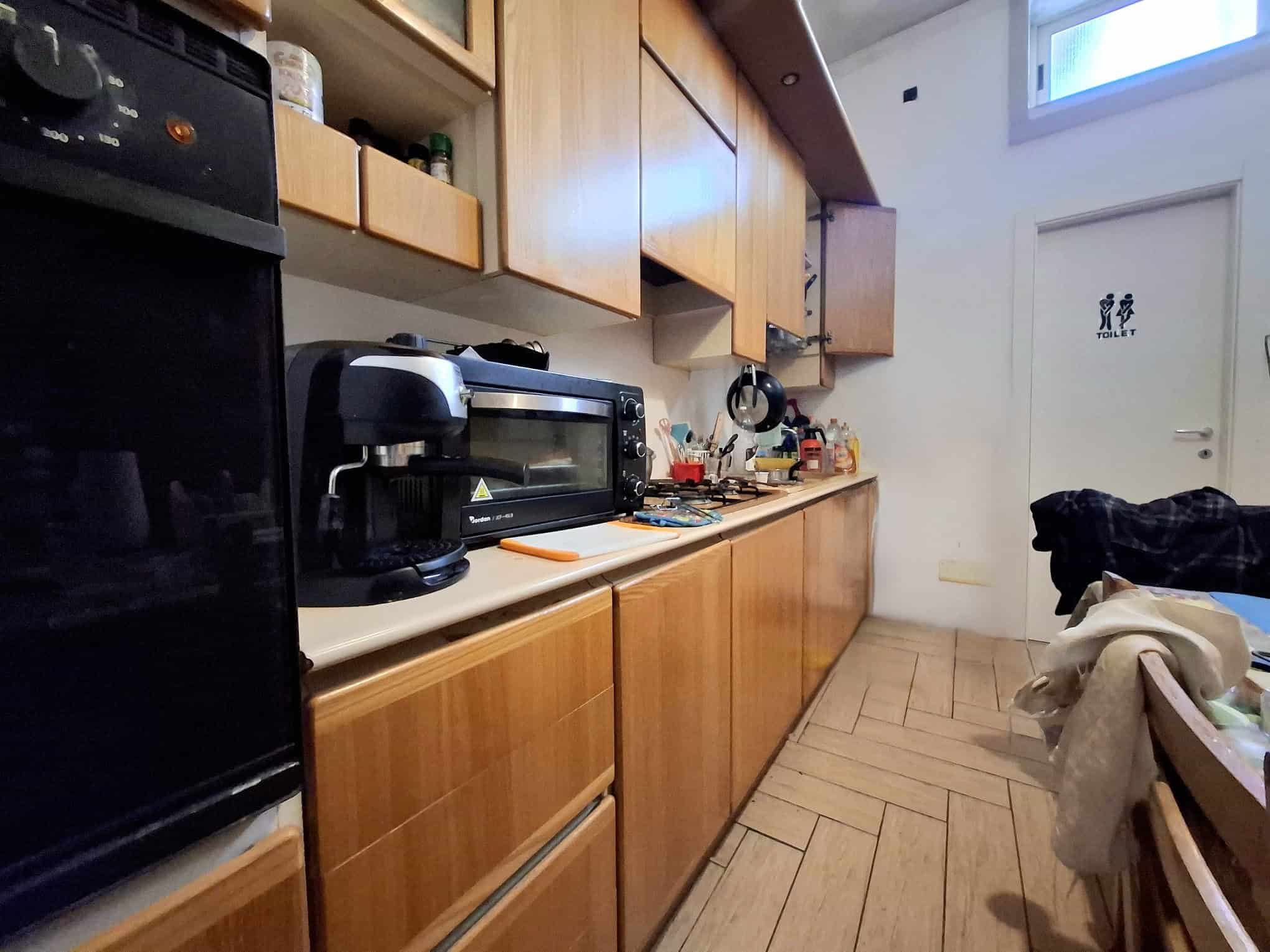 Lavagna da cucina moderna con mobili in legno chiaro, elettrodomestici e utensili, ambiente luminoso e funzionale per preparare i pasti.