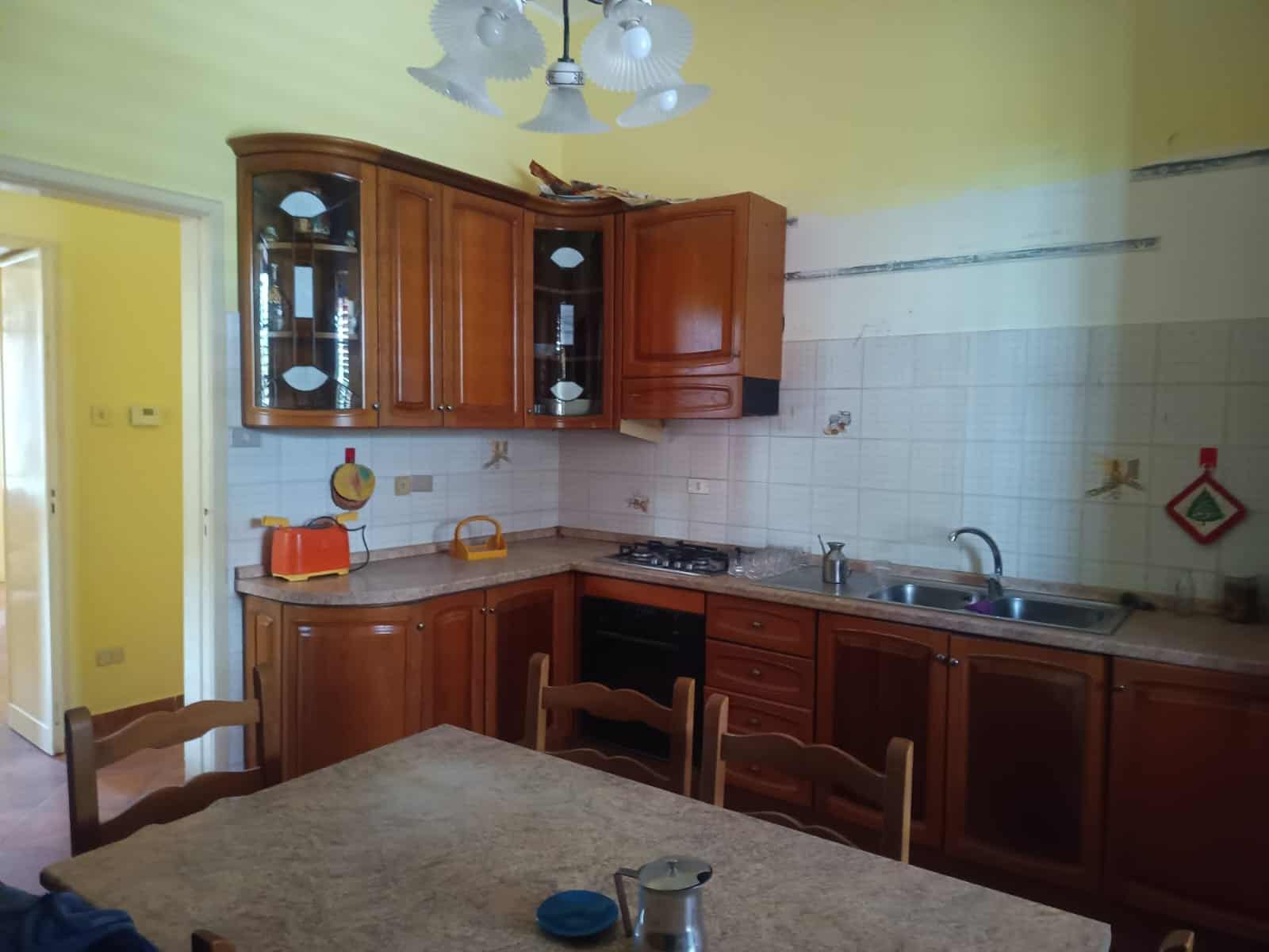 Pannello cucina in legno con mobili classici, piano cottura e lavello in acciaio, ambiente abitabile e funzionale, ideale per ristrutturare o arredare la tua casa con stile tradizionale.