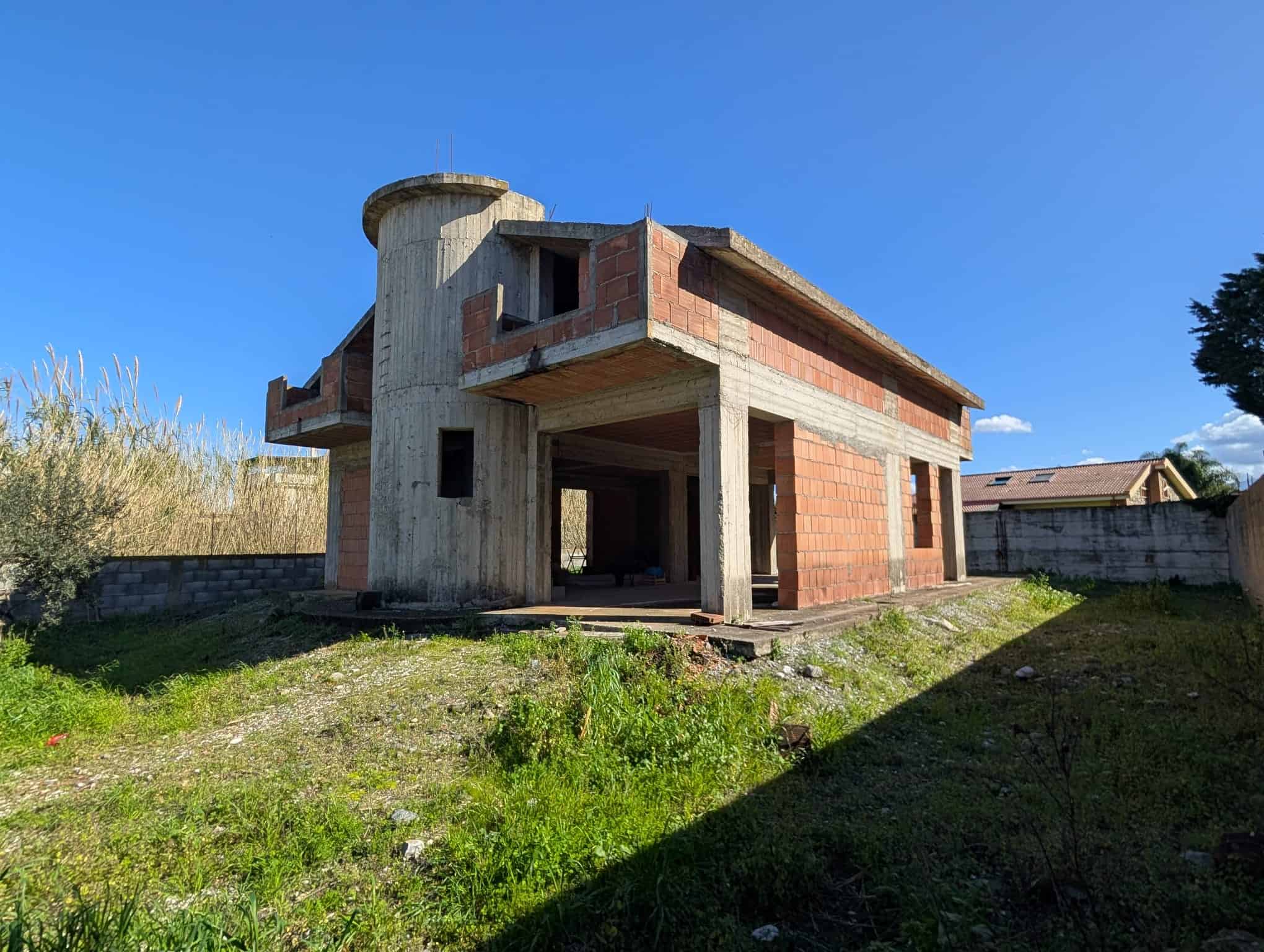 Pannello di costruzione di una casa in fase di sviluppo con struttura in cemento e mattoni, situata in un'area verde soleggiata e aperta, pronta per essere completata.