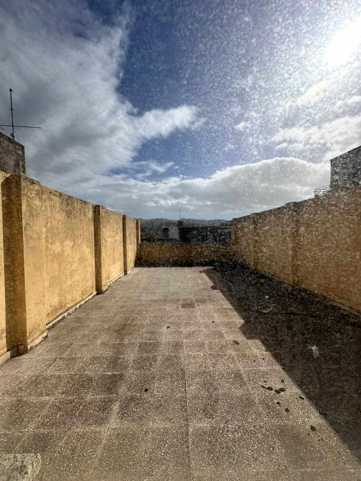 Balcone con vista panoramica e cielo nuvoloso, pavimentato in pietra, con muri in pietra e un'antenna sullo sfondo, ideale per attività all'aperto e relax all'aperto.