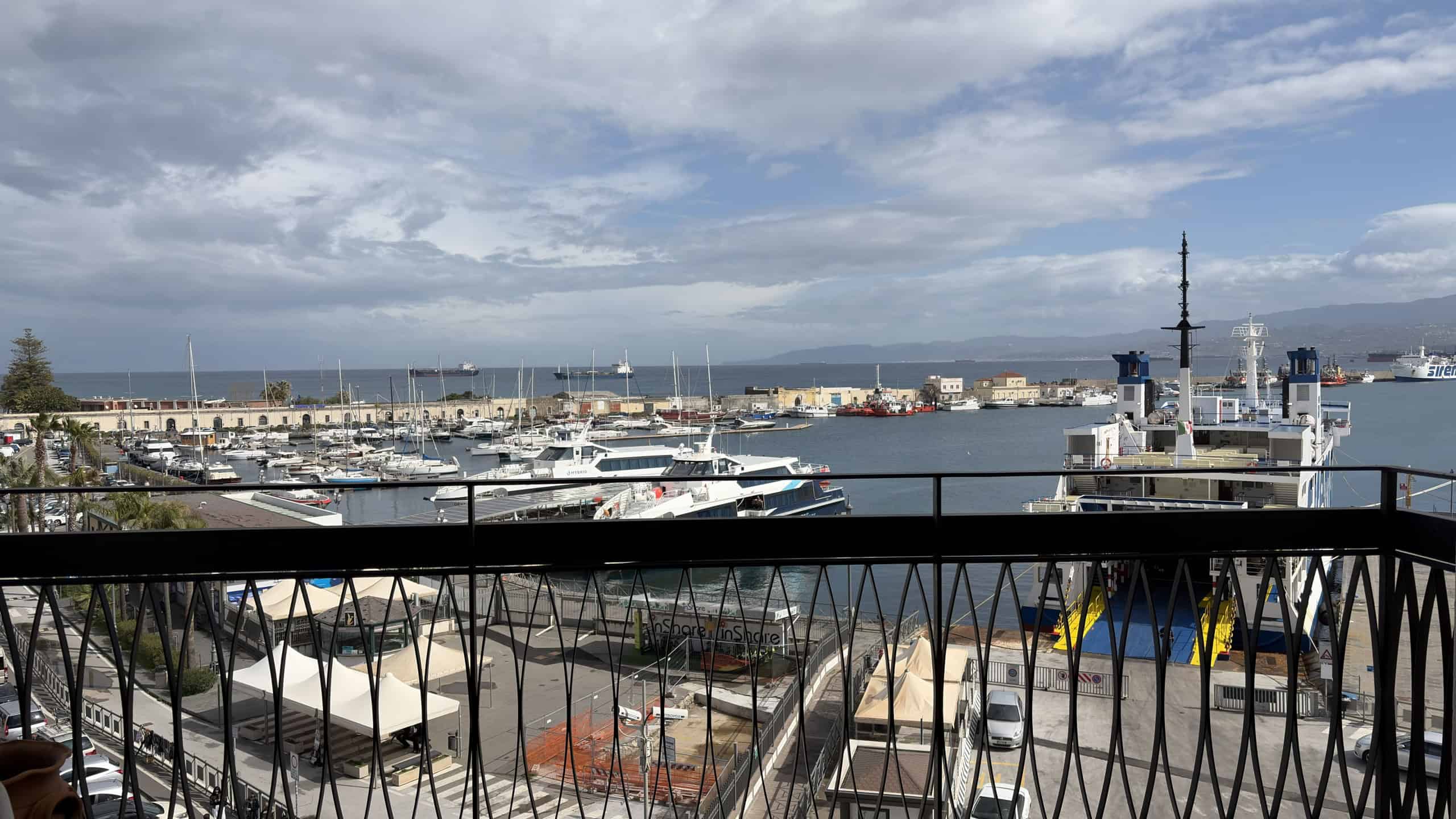 Vista panoramica del porto con yacht e imbarcazioni, cielo nuvoloso e skyline urbano sullo sfondo, vista dal balcone di un appartamento a NextCasa, zona marina e turistica.