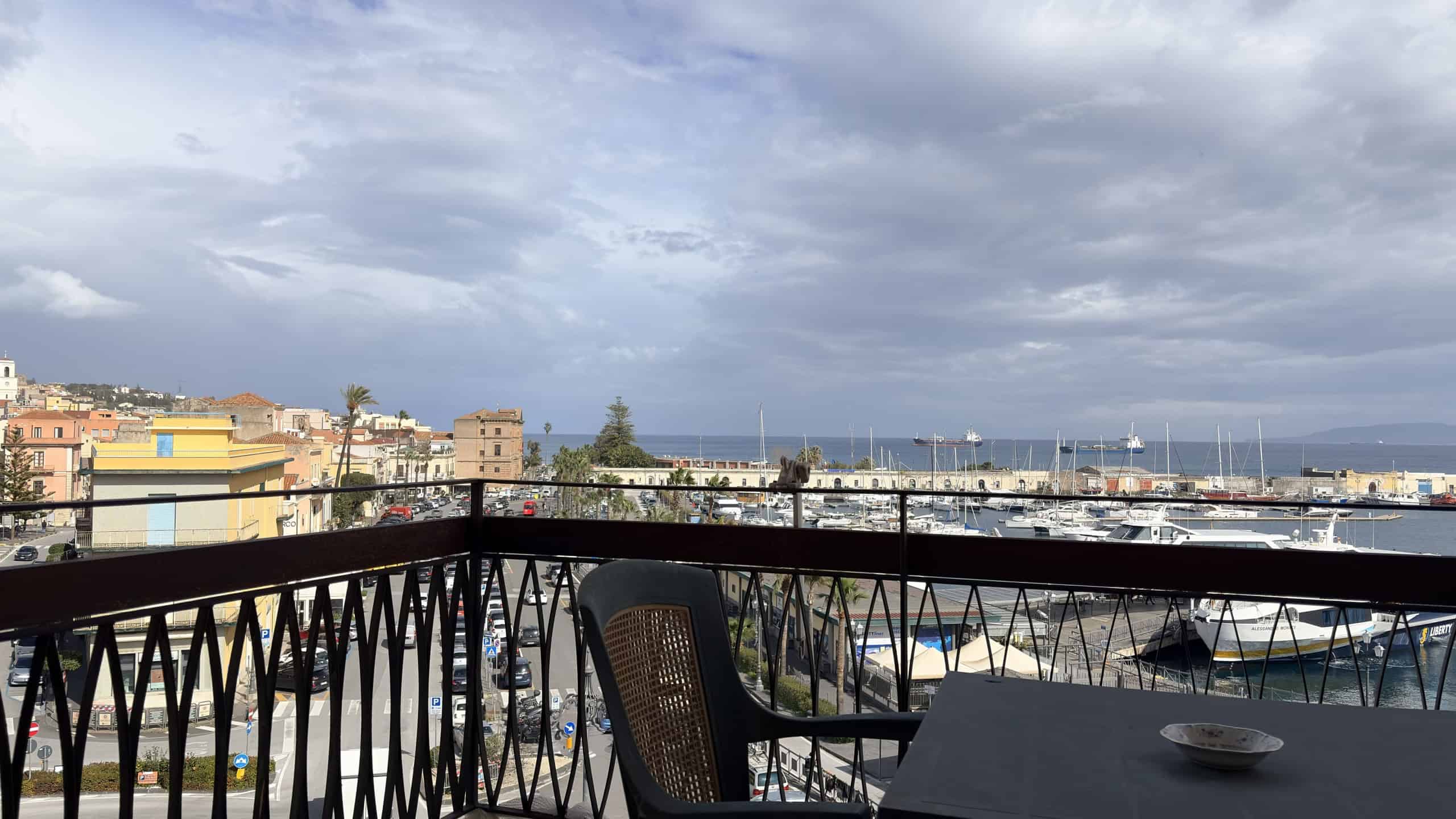 Balcone con vista sul porto e sulla città, cielo nuvoloso, in un appartamento moderno a NextCasa, soluzione ideale per vivere vicino al mare e alle attrazioni urbane.