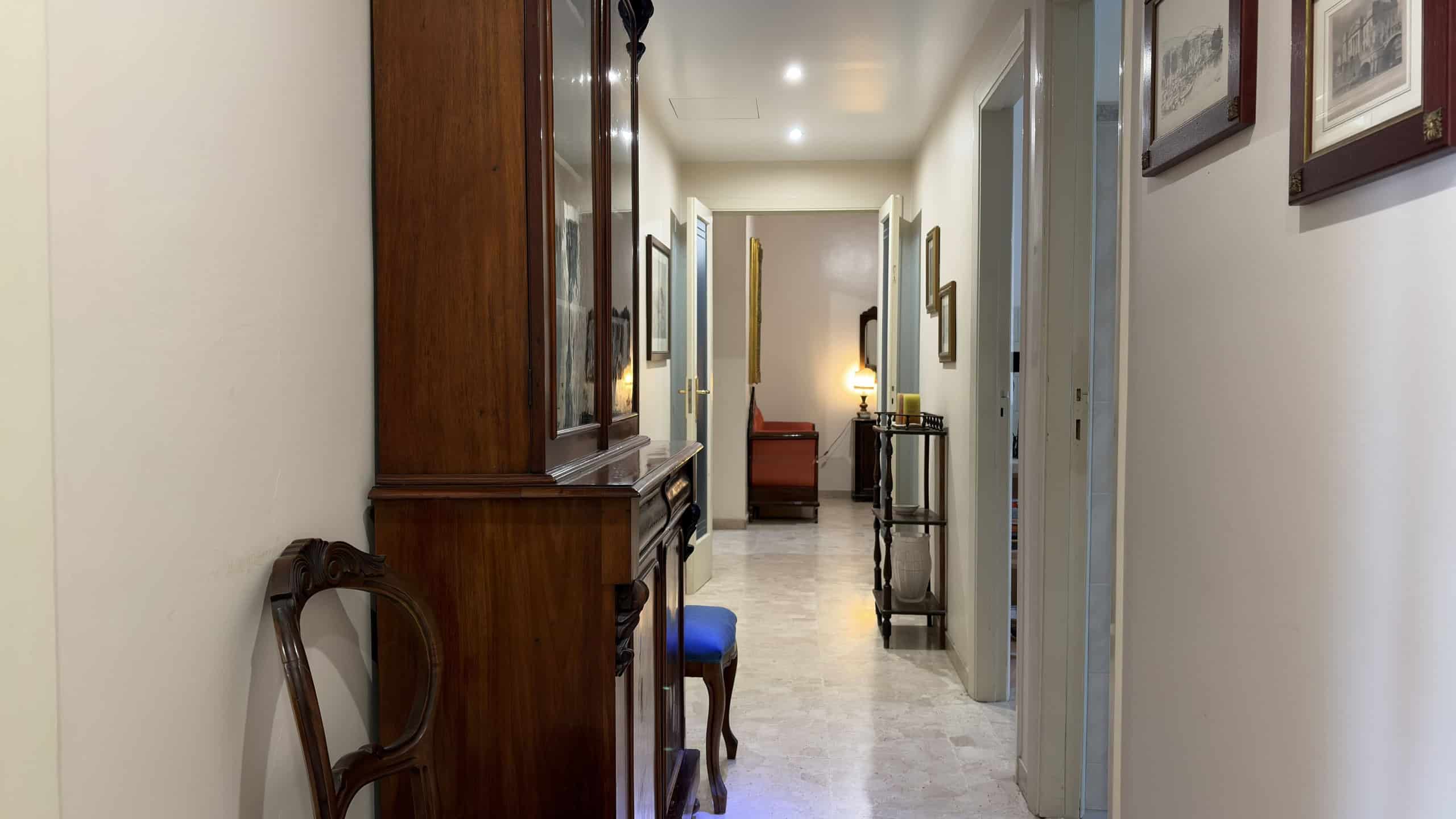 Elegante corridoio interno di una casa moderna con pareti decorate e mobili in legno, ideale per servizi di intermediazione immobiliare e affitti di case di lusso.