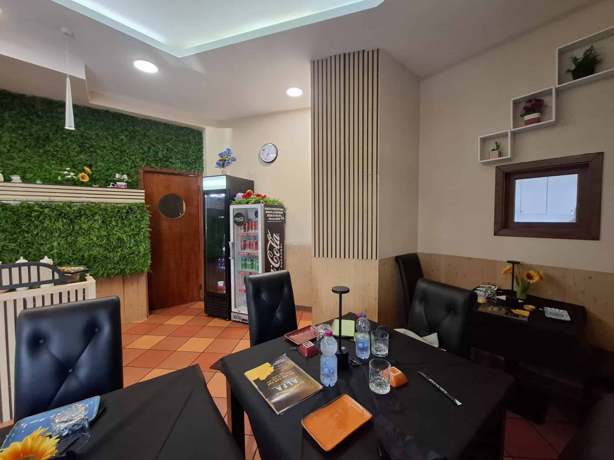 Ampia sala da pranzo moderna con pareti decorate con piante verdi e mobili eleganti, ideale per incontri sociali e cene conviviali. Atmosfera accogliente e luminosa, perfetta per momenti di relax e co.