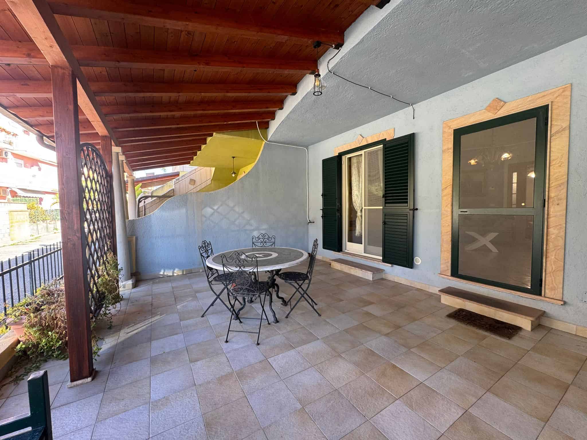 Ampia terrazza esterna con tavolo e sedie, ideale per relax e cene all'aperto, con copertura in legno e vista sul giardino, perfetta per vivere all'aperto in un ambiente accogliente e funzionale.