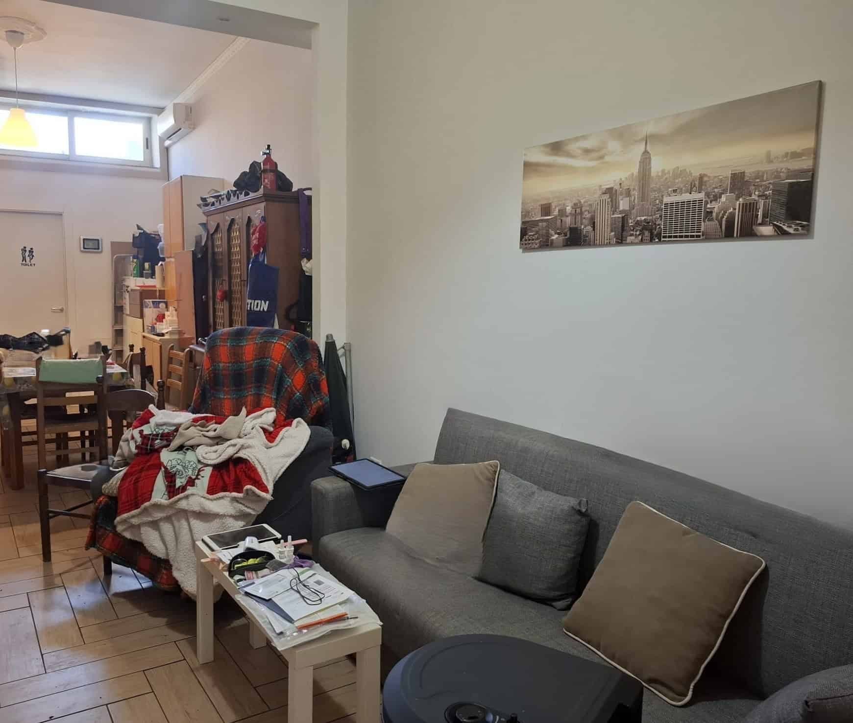 Appartamento accogliente con soggiorno arredato con divano, cuscini e tavolino, decorato con una foto panoramica di New York sulla parete, in un ambiente luminoso e confortevole.