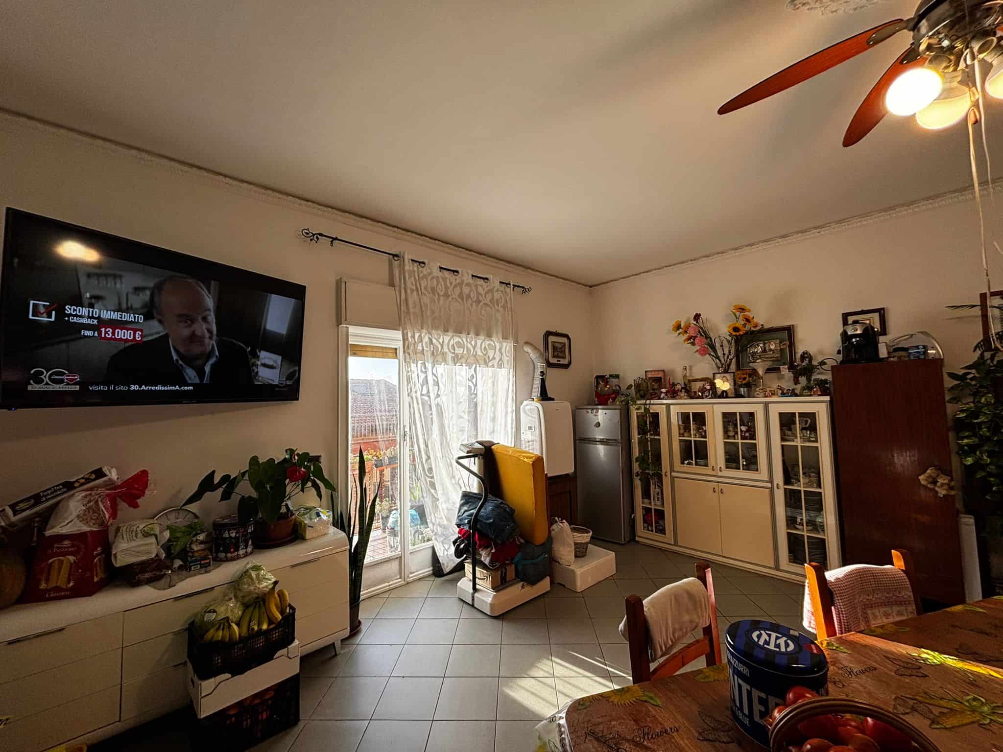 Il soggiorno di una casa moderna con mobili funzionali, TV a schermo piatto, e decorazioni floreali, ideale per vivere momenti di relax e convivialità. Spazio luminoso e accogliente, perfetto per fami.