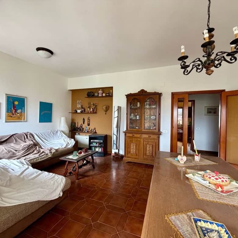 Ampia sala soggiorno con mobili classici, tavolo in legno, armadio antico e decorazioni eleganti, ambiente luminoso e accogliente, ideale per vivere momenti di relax e convivialità.