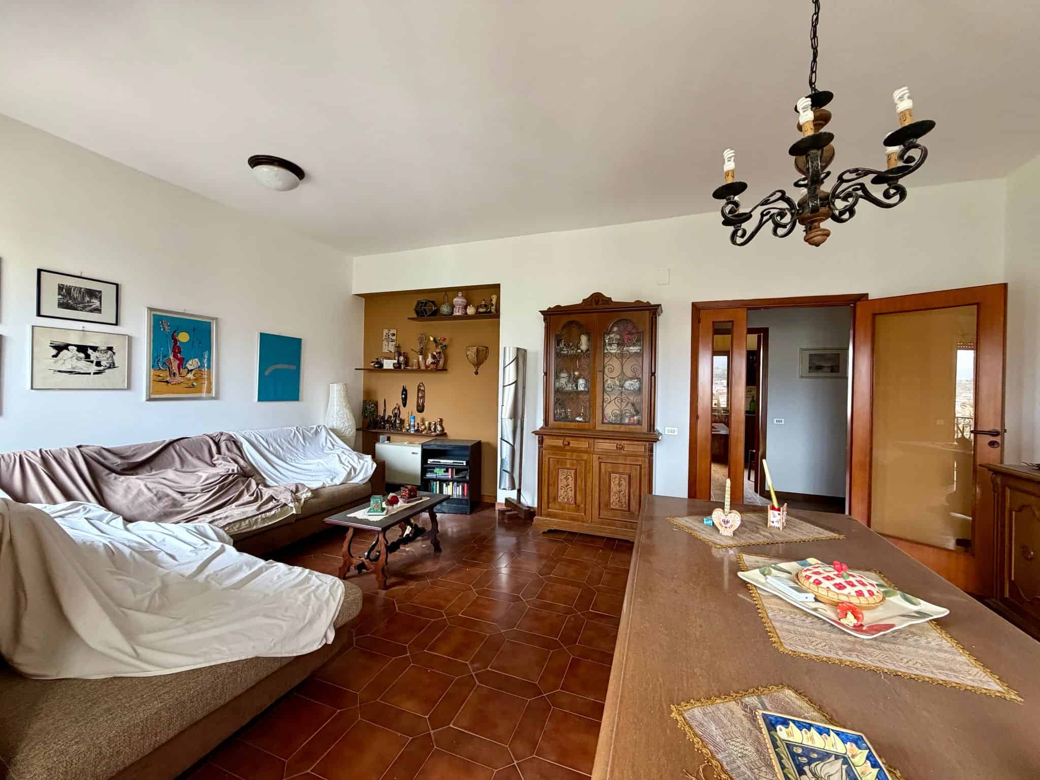 Ampia sala soggiorno con mobili classici, tavolo in legno, armadio antico e decorazioni eleganti, ambiente luminoso e accogliente, ideale per vivere momenti di relax e convivialità.