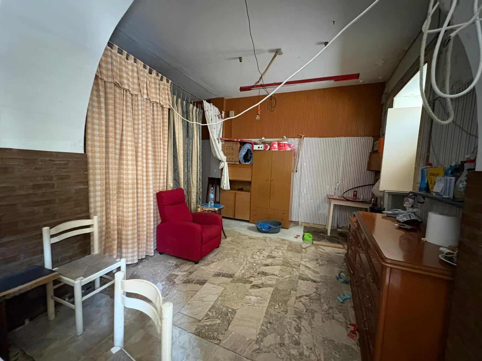 Interno di una casa disordinata con mobili vecchi, tende e cavi pendenti, ambiente trascurato e poco illuminato, ideale per servizi di ristrutturazione o pulizia approfondita.
