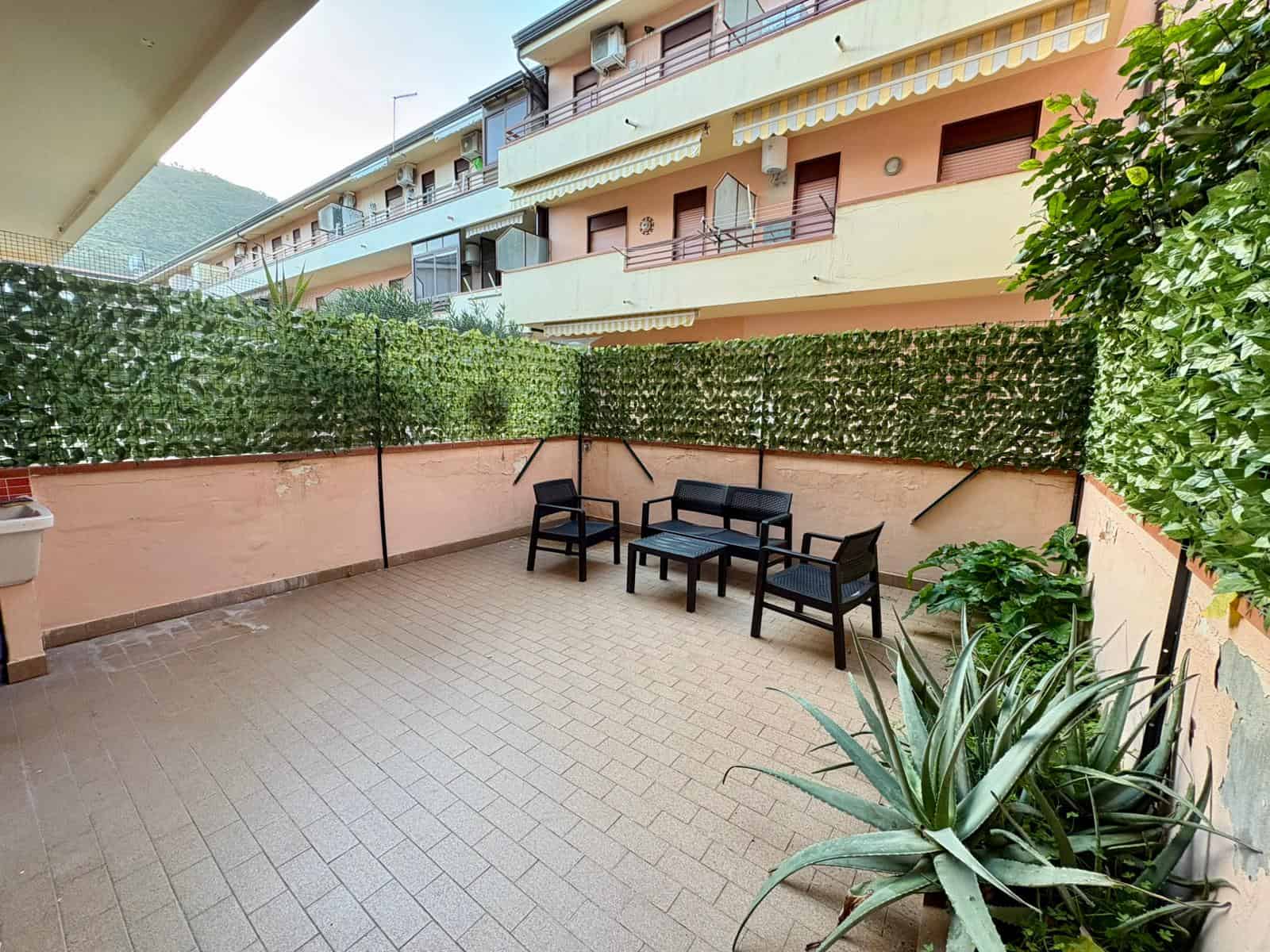Ampia terrazza privata con arredi da esterno, piante verdi e vista sulle palazzine circostanti, ideale per relax e convivialità all'aperto.