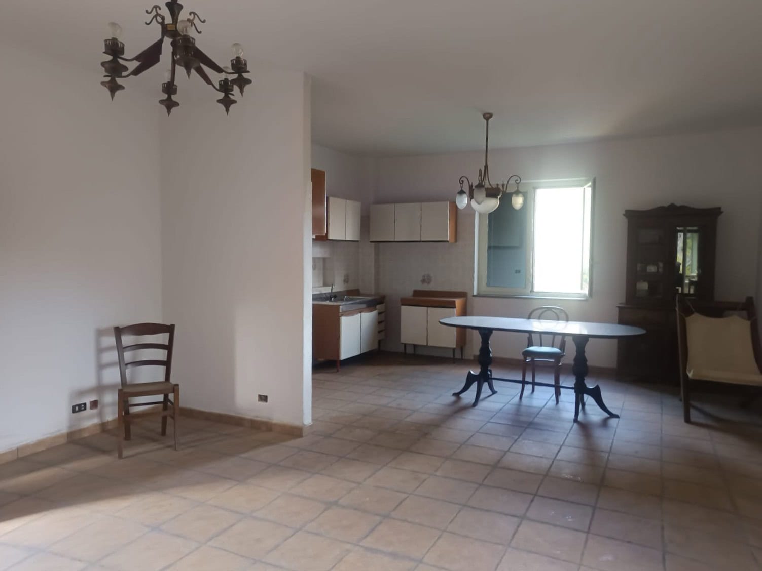 Interno spazioso di una casa con cucina e zona pranzo, arredamento classico, illuminazione naturale, pavimento in piastrelle beige, ambiente luminoso e accogliente.