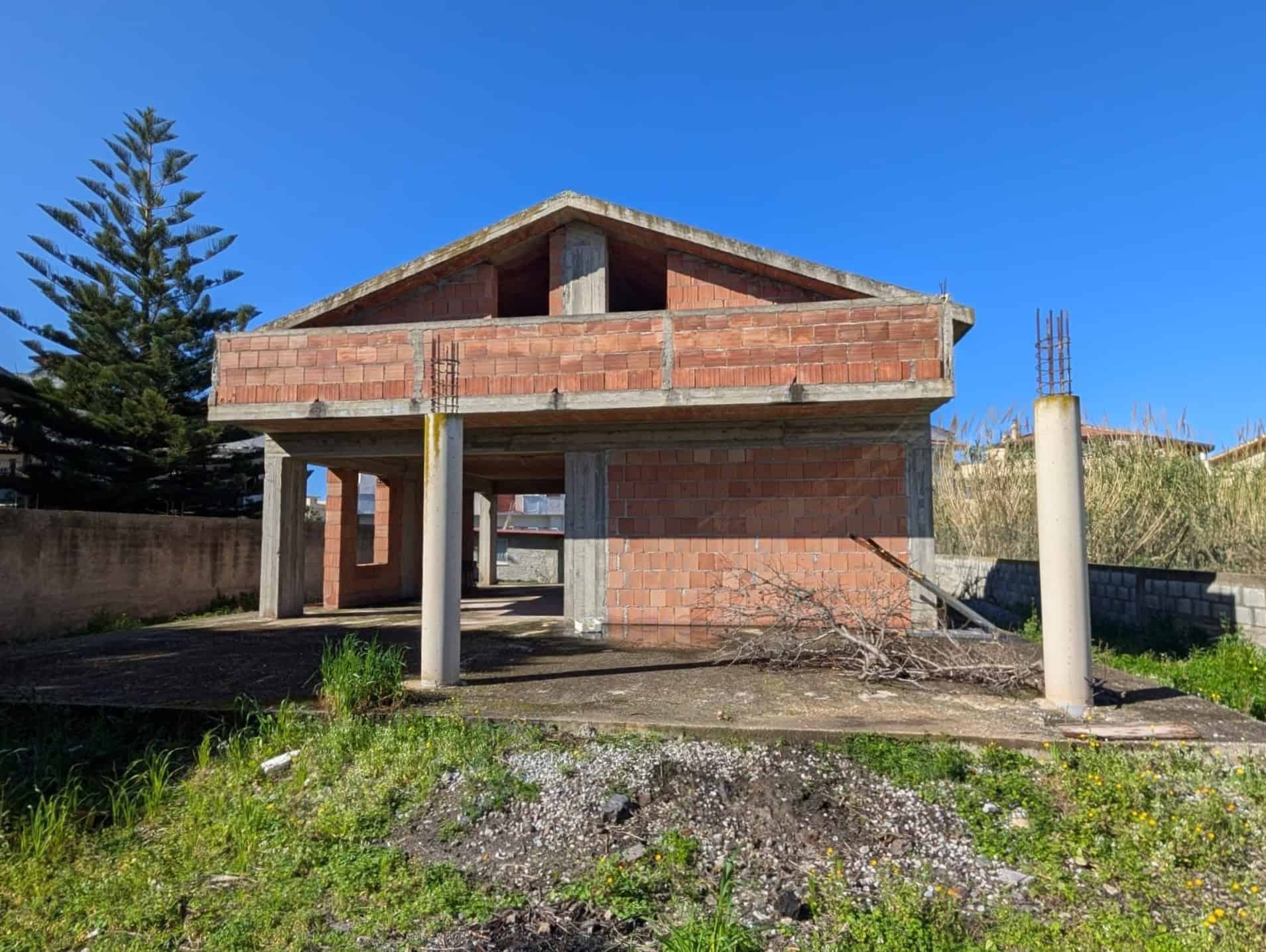 Scorcio di una casa in costruzione con struttura in cemento e mattoni, pronta per essere rifinita, sotto un cielo azzurro e con vegetazione circostante.