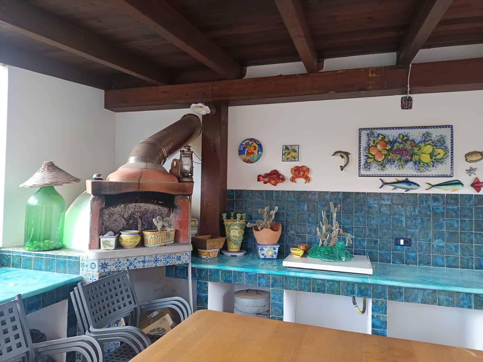 Un forno a legna in stile rustico con pareti decorate con piastrelle blu e oggetti marini, ideale per cucinare e creare un'atmosfera accogliente in casa.