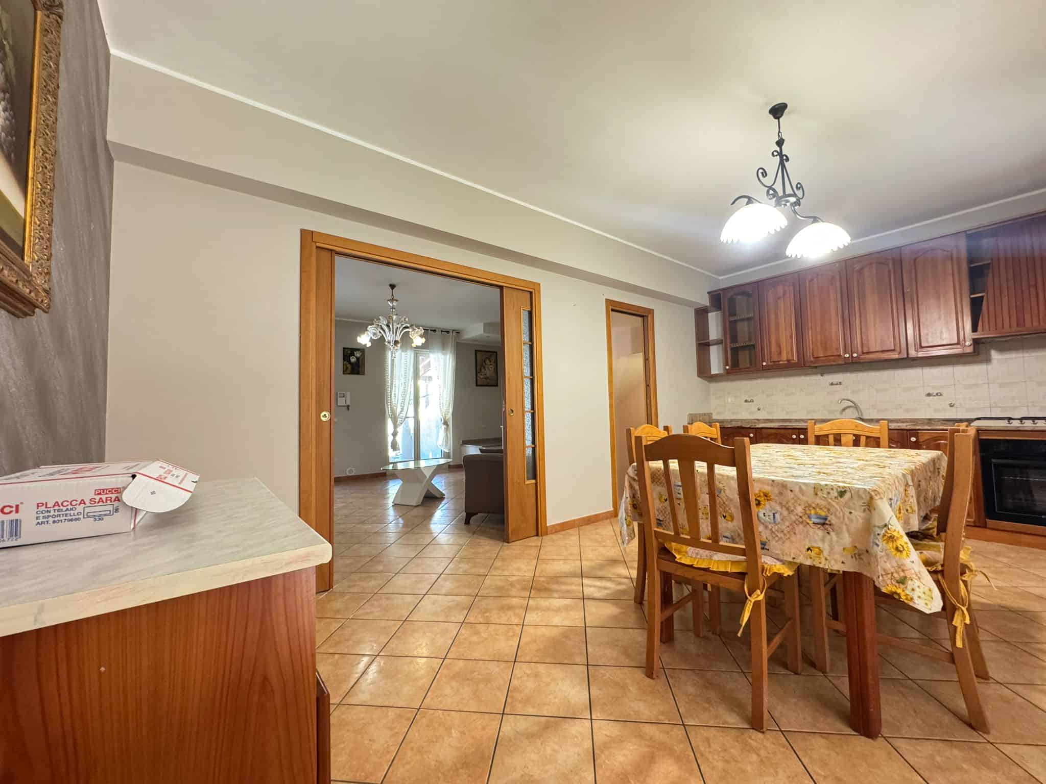Ampio soggiorno con zona pranzo e cucina in stile classico, arredamento in legno e illuminazione centrale, ideale per famiglie e convivialità.